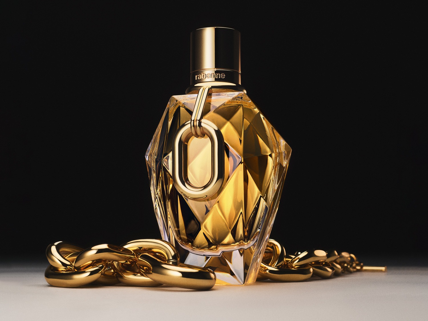 Zlatistý flakón parfumu Rabanne zdobený zlatou retiazkou, ktorý evokuje luxus a eleganciu.