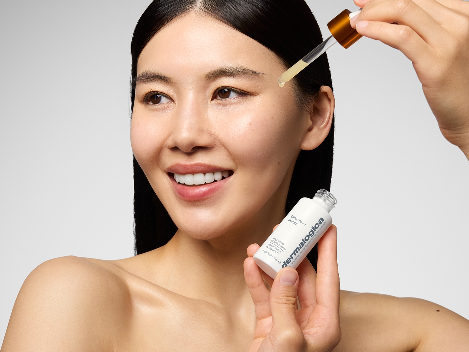 Een stralende vrouw gebruikt Dermalogica Biolumin-C Serum met een pipet om haar huid te verhelderen.