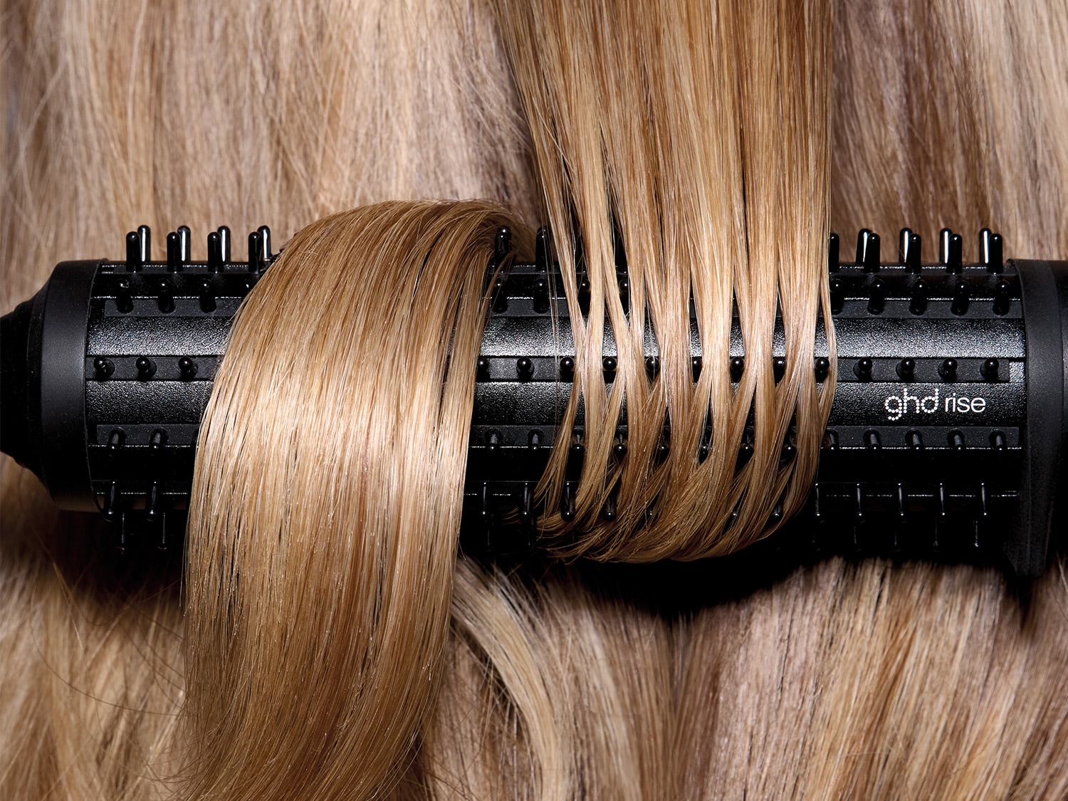 Nahaufnahme von blondem Haar, das um eine schwarze ghd Rise-Rundbürste gewickelt ist, um Volumen und Schwung zu erzeugen.