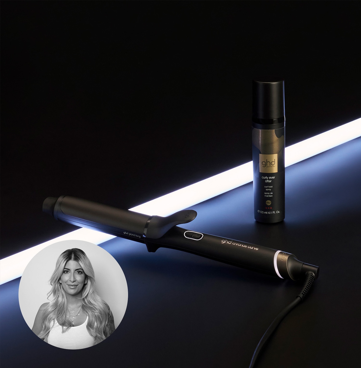 GHD Grand Tong Lockenstab und eine schwarze Sprühflasche GHD Curly Ever After Curl Hold Spray liegen vor einer hellen Neonröhre, während ein Porträt einer blonden Frau in einem Kreis zu sehen ist.
