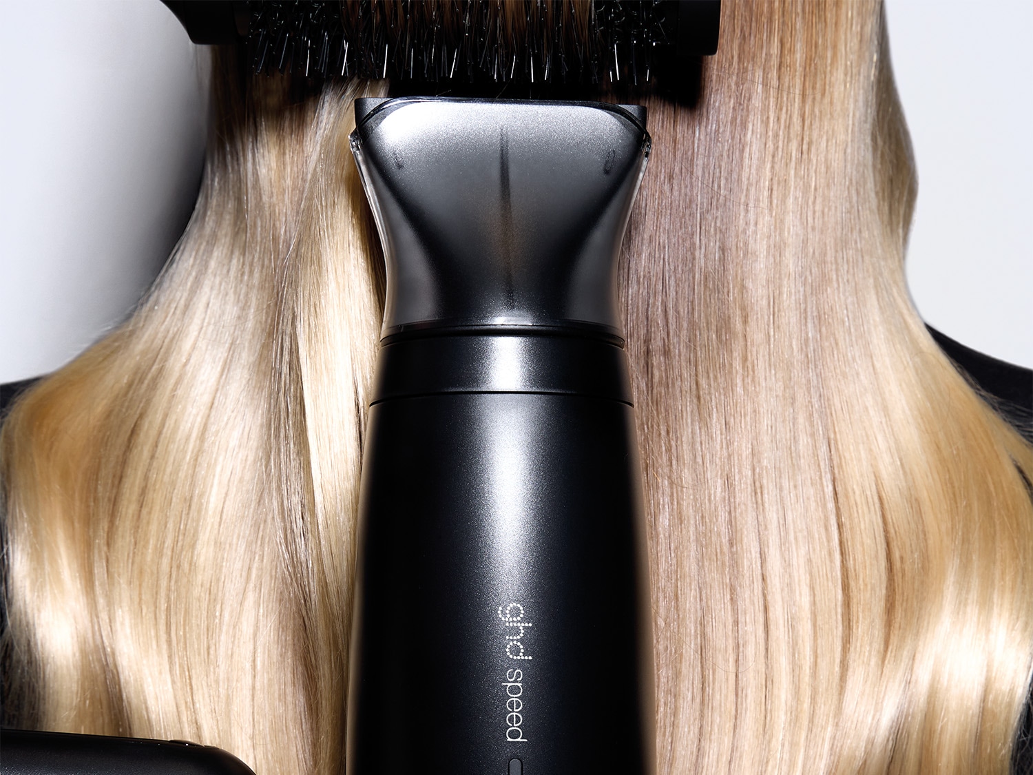 Ein schwarzer ghd Speed Haartrockner wird verwendet, um blondes, langes Haar mit einer Bürste zu stylen.