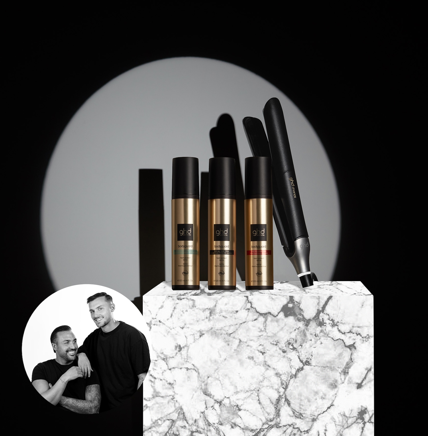 Drei goldene ghd Bodyguard Hitzeschutzsprays und ein ghd Chronos Glätteisen stehen auf einem Marmorwürfel, während ein Porträt von zwei Männern im Kreis links unten zu sehen ist.