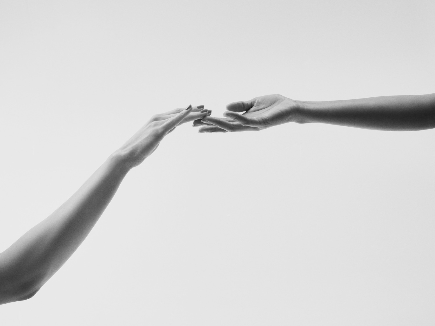 Due mani si protendono l'una verso l'altra, quasi a toccarsi, su uno sfondo bianco, creando un'immagine di connessione e delicatezza.