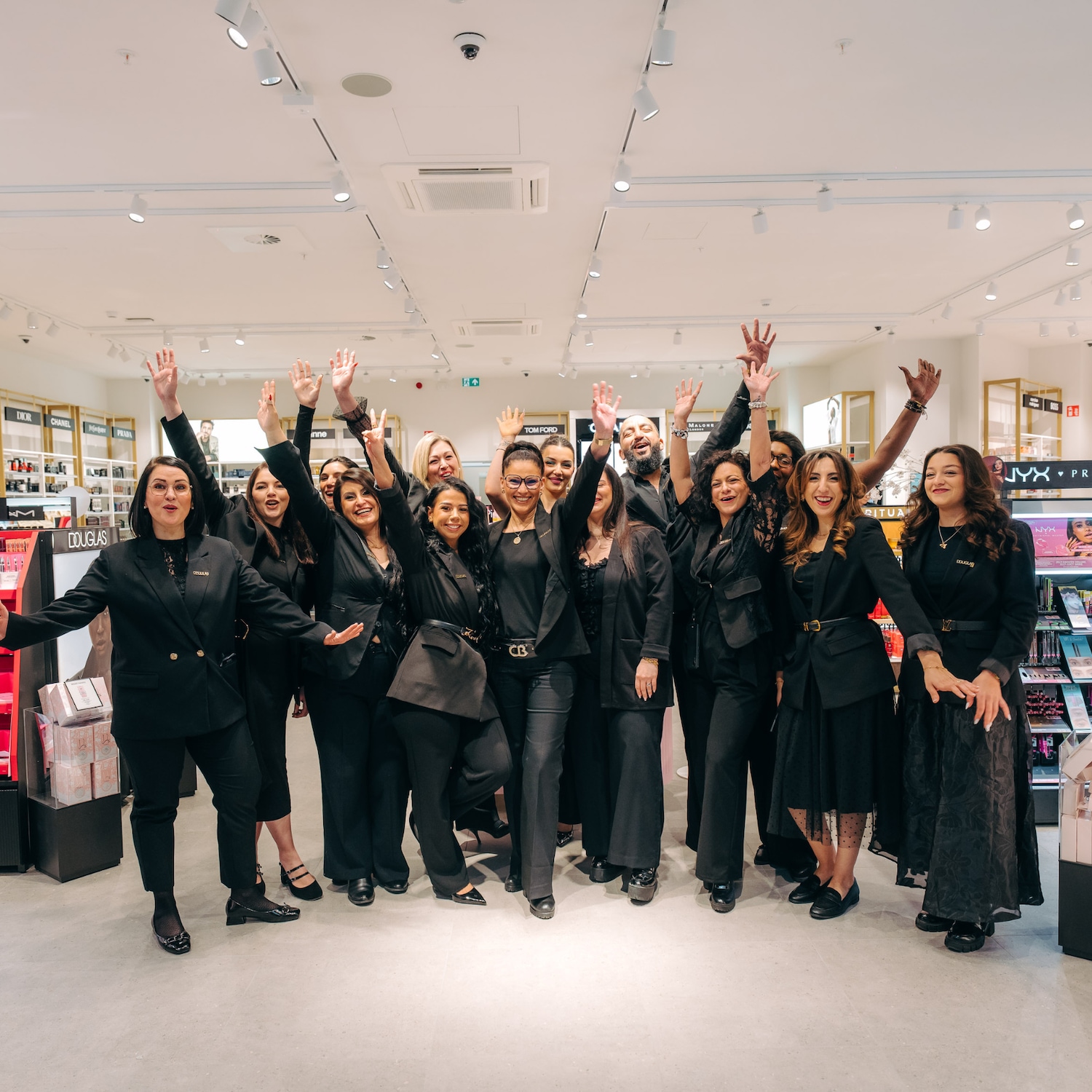 Un groupe diversifié d'employés de Douglas, vêtus de noir, célèbrent avec les bras levés dans un magasin bien éclairé, reflétant un esprit d'équipe et de joie.