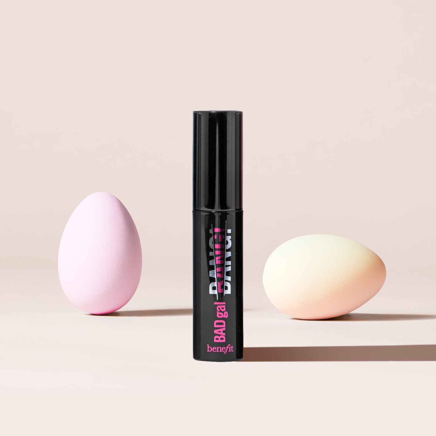 Benefit BADgal BANG! Mascara in schwarzer Tube mit pinkfarbenem Aufdruck, flankiert von pastellfarbenen Ostereiern.