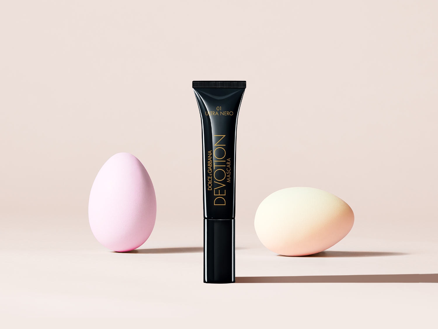 Dolce & Gabbana Devotion Mascara in schwarzer Tube mit goldenen Akzenten, umgeben von pastellfarbenen Ostereiern.