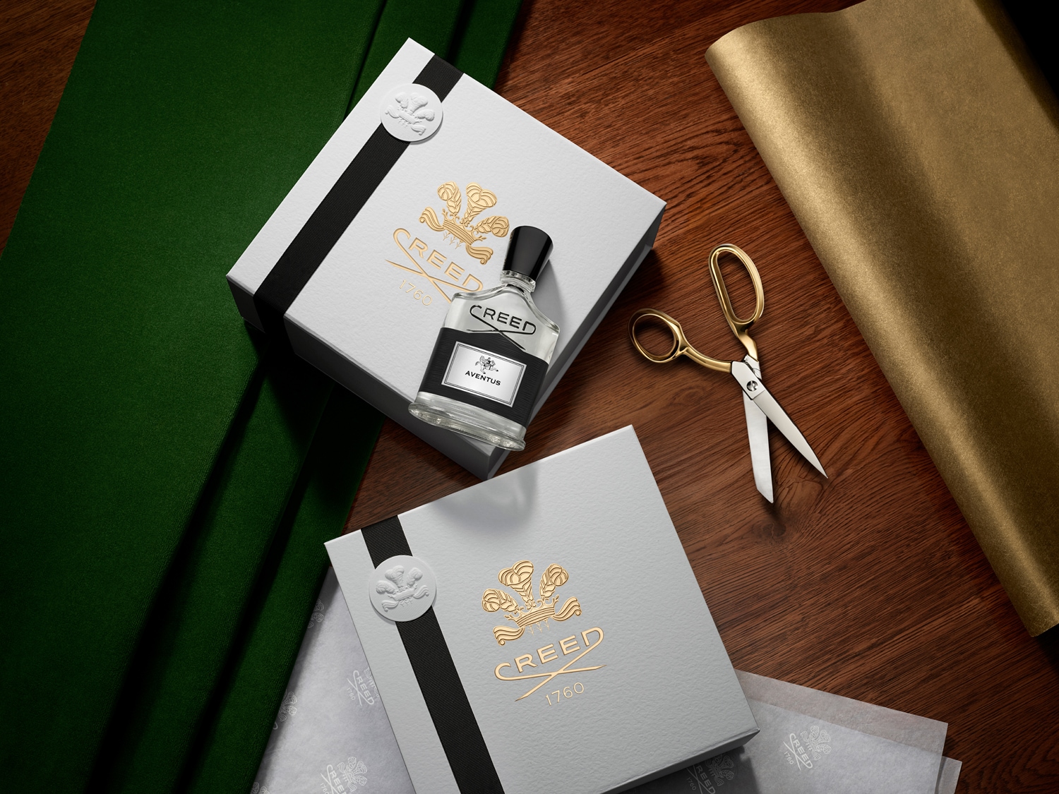 Elegantní balení parfému Creed Aventus s bílou krabičkou, černou stuhou a zlatým logem, doplněné o zlaté nůžky a balicí papír.