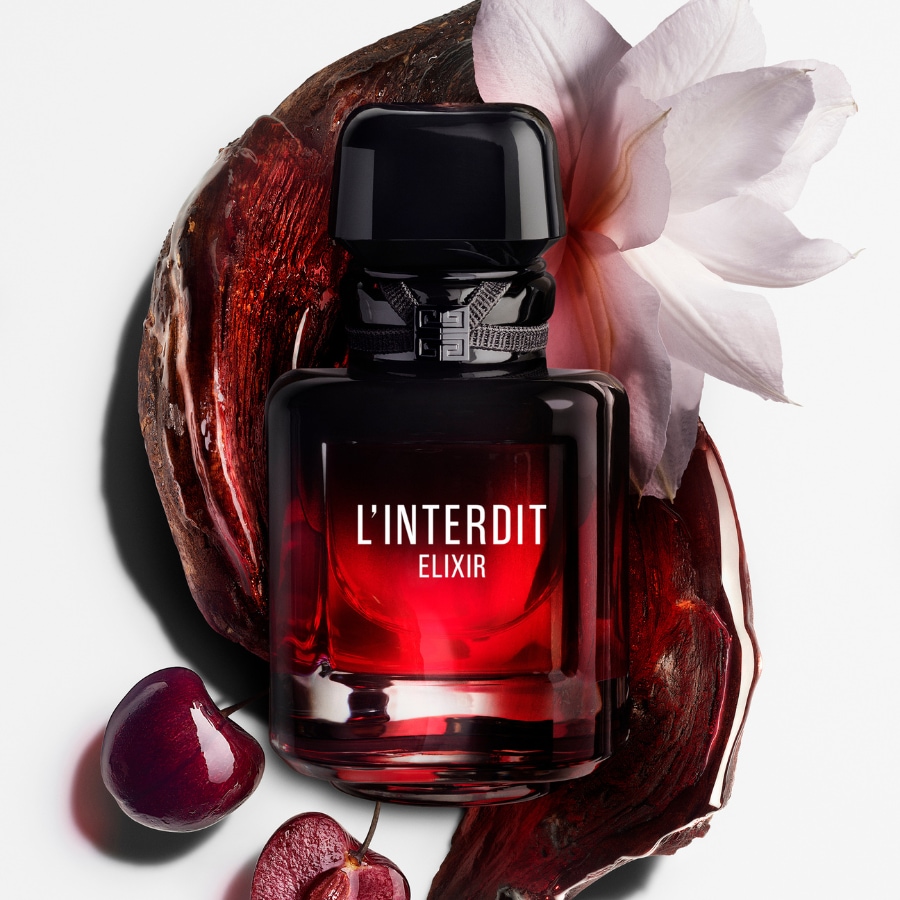 Der L'Interdit Elixir Duft von Givenchy ist in einem eleganten, schwarz-roten Flakon mit einem schwarzen Verschluss und einem Band mit dem Markenlogo erhältlich, umgeben von einer weißen Blüte, Kirschen und dunklen Holzstücken.