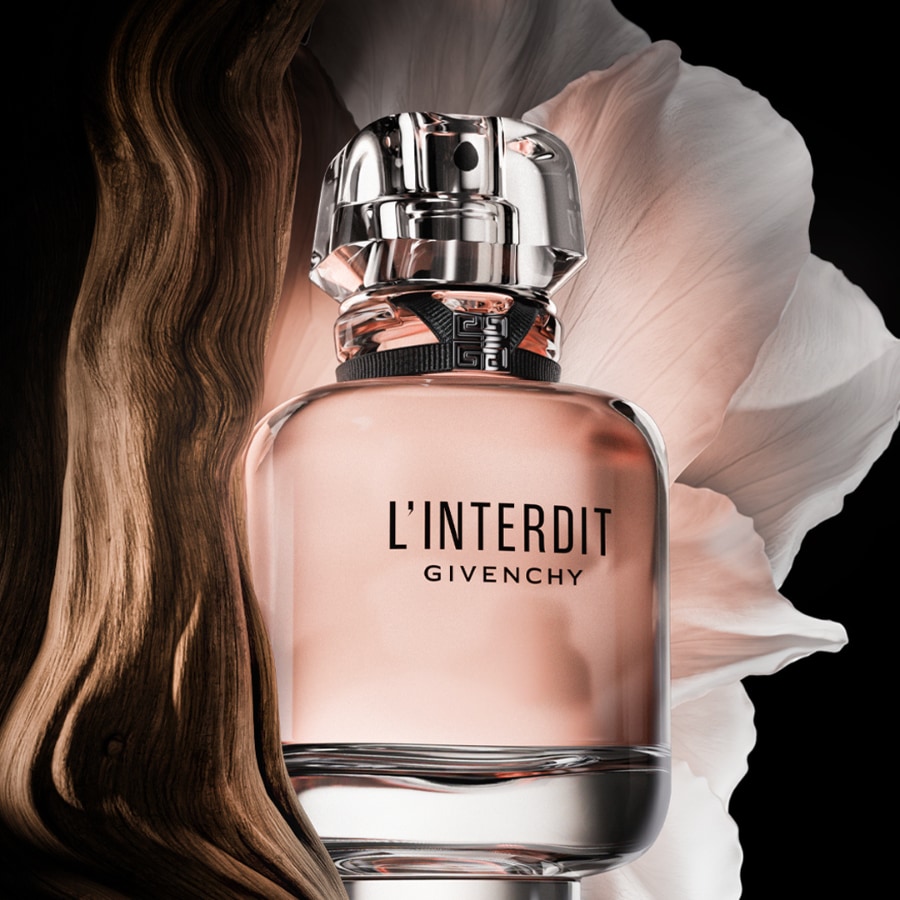 Der L'Interdit Givenchy Duft in einem eleganten, transparenten Flakon mit rosafarbenem Inhalt und silbernem Verschluss, umgeben von einem dunklen Holzelement und einem zarten, hellen Blütenblatt auf schwarzem Hintergrund.