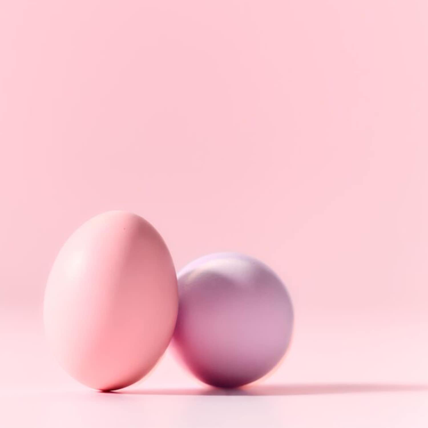 Twee zachtroze en lila paaseieren staan tegen een roze achtergrond, klaar om Pasen te vieren.