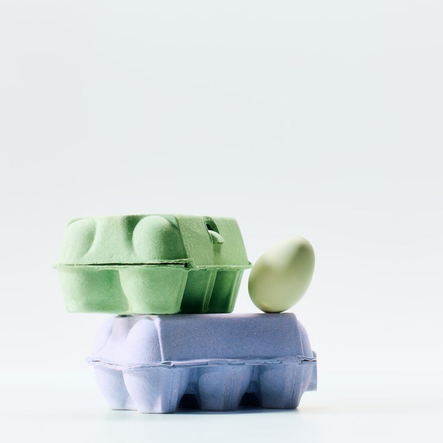 Twee gekleurde eierdozen, een groene bovenop een blauwe, met een groen ei dat ertegenaan leunt.