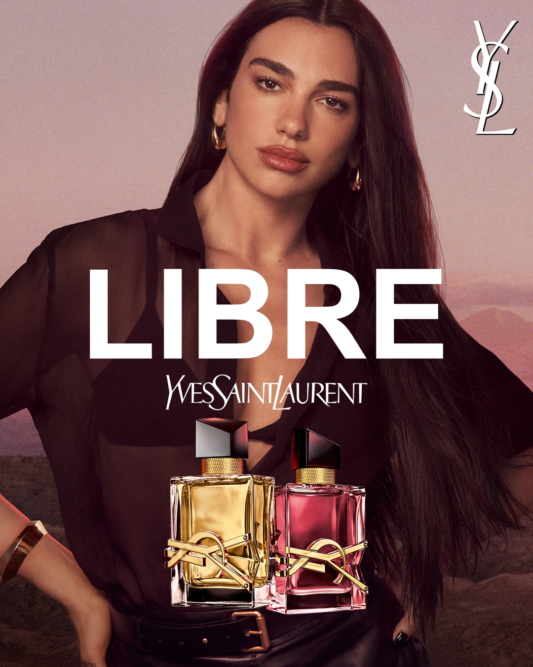 Na tle kobiety w czarnej bluzce widnieją dwa flakony perfum Yves Saint Laurent Libre, jeden ze złotą, a drugi z różową zawartością, oba z czarnymi korkami i złotym logo.