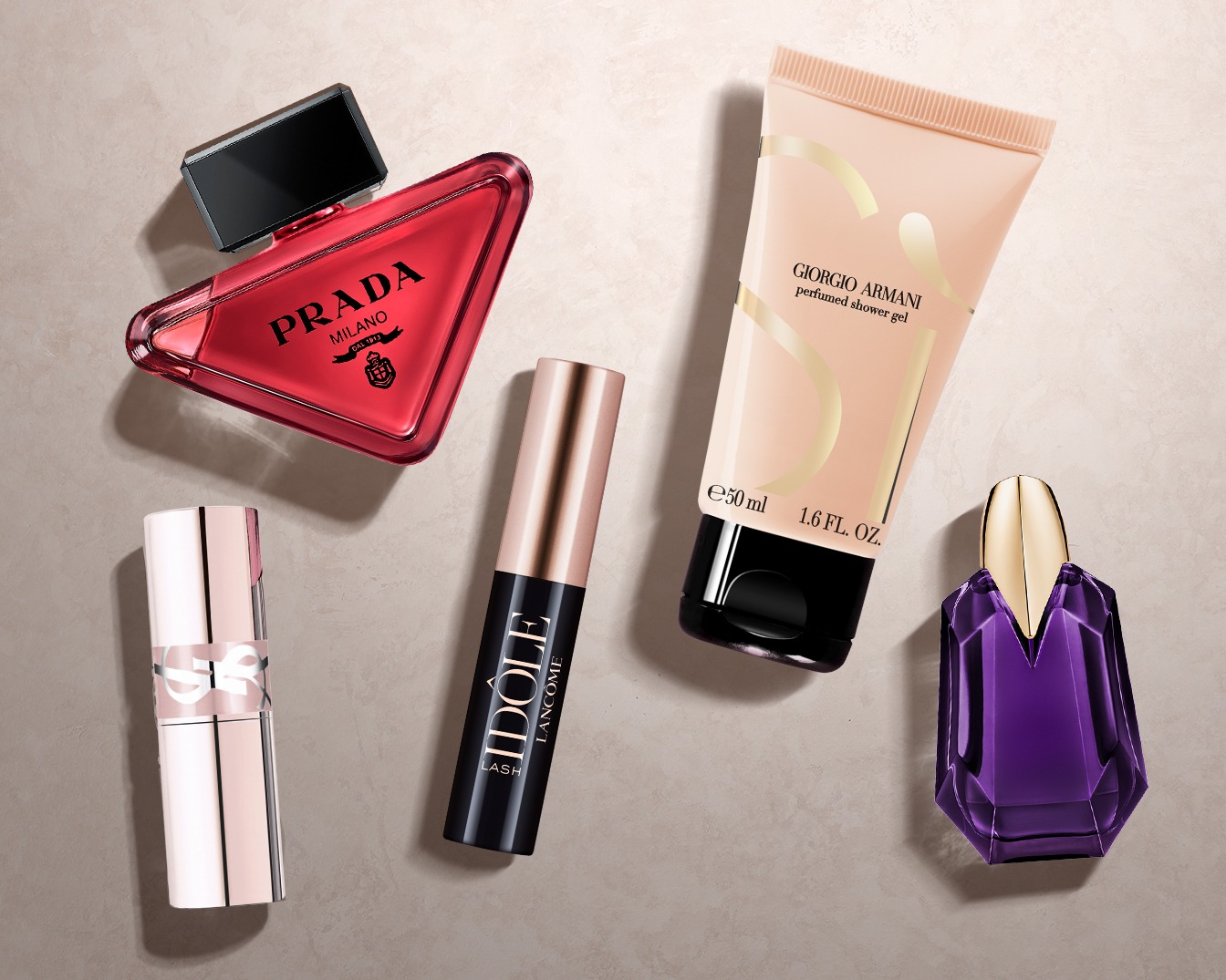 Ontdek een collectie van luxe schoonheidsproducten, waaronder een rode Prada-parfum, Lancôme Idôle Lash-mascara, Giorgio Armani-douchegel, een paarse Alien-parfum en een YSL-lipstick.