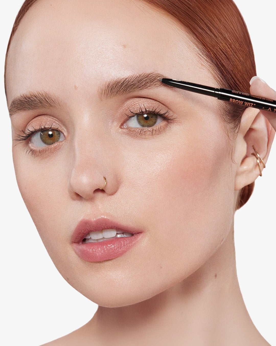 Nahaufnahme einer Frau mit roten Haaren, die mit dem Augenbrauenstift Anastasia Beverly Hills Brow Wiz ihre Augenbrauen nachzeichnet.