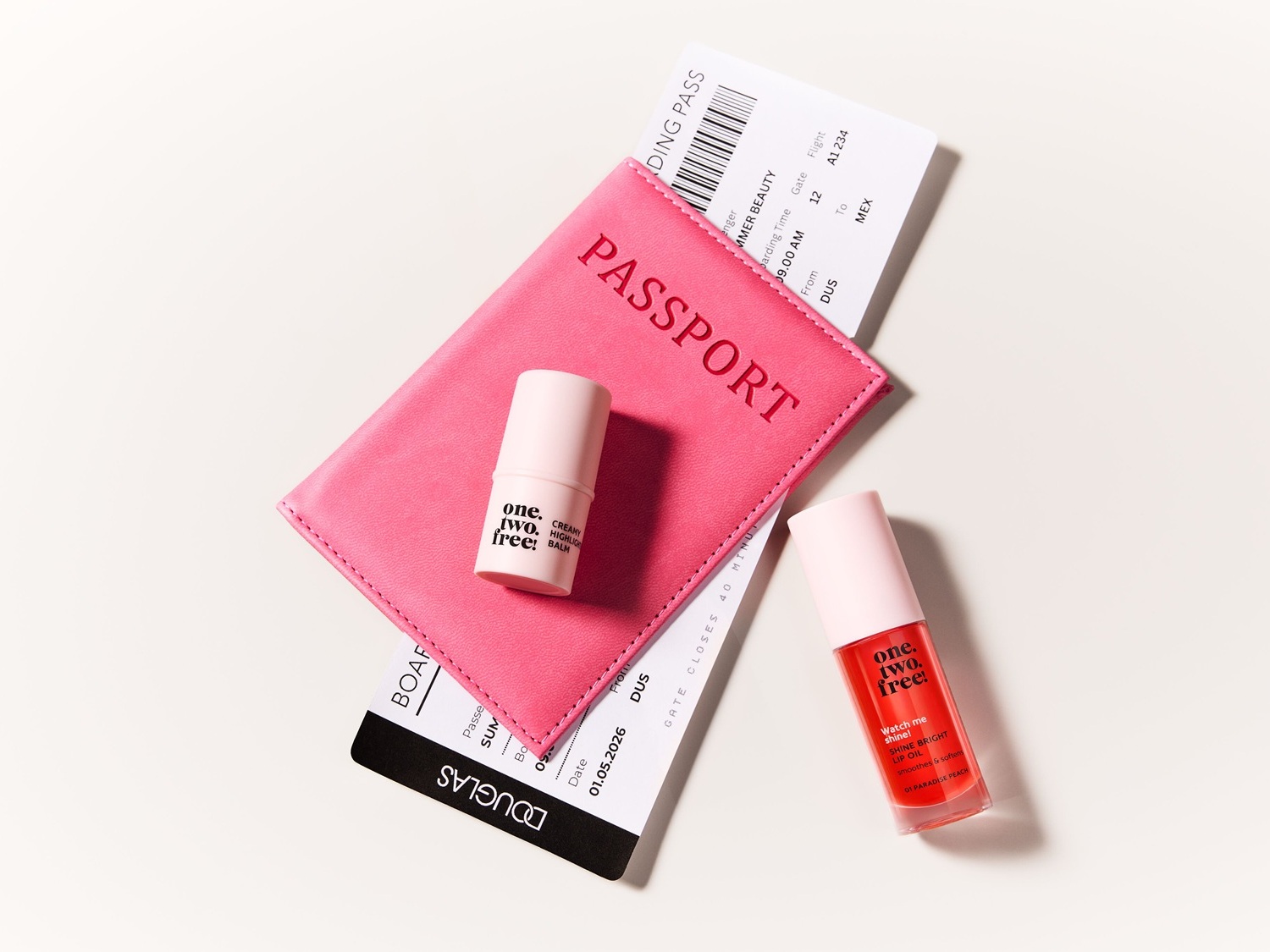 Ecco un set di bellezza da viaggio con un passaporto rosa, una carta d'imbarco e due prodotti di bellezza "one. two. free!".