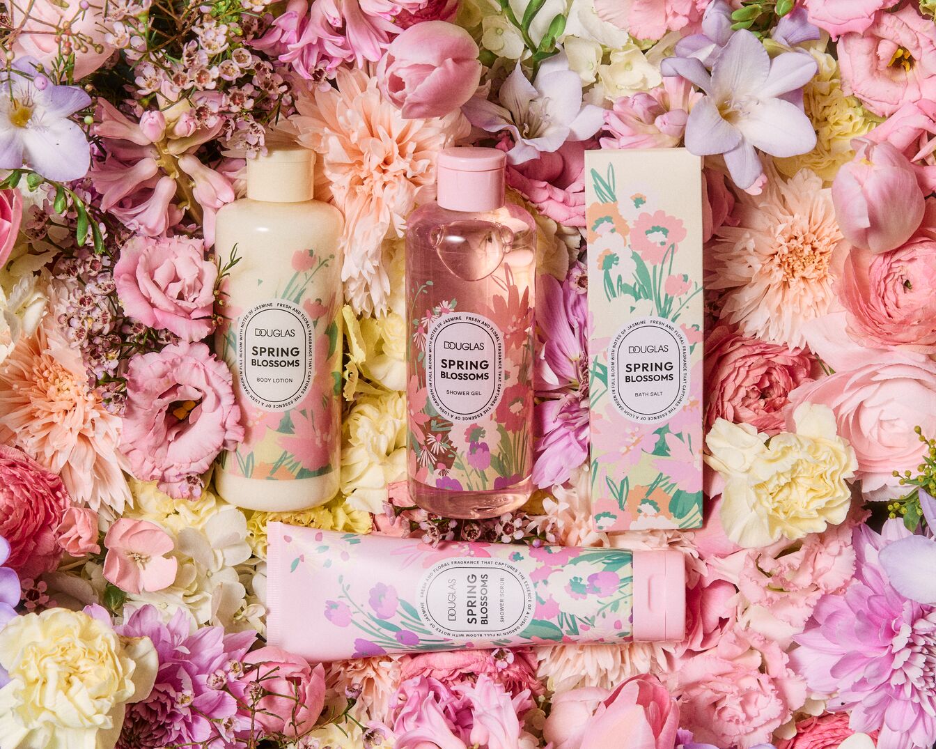 Vier Douglas Spring Blossoms producten, waaronder bodylotion, douchegel, badzout en een douchescrub, liggen tussen een bed van roze en witte bloemen.