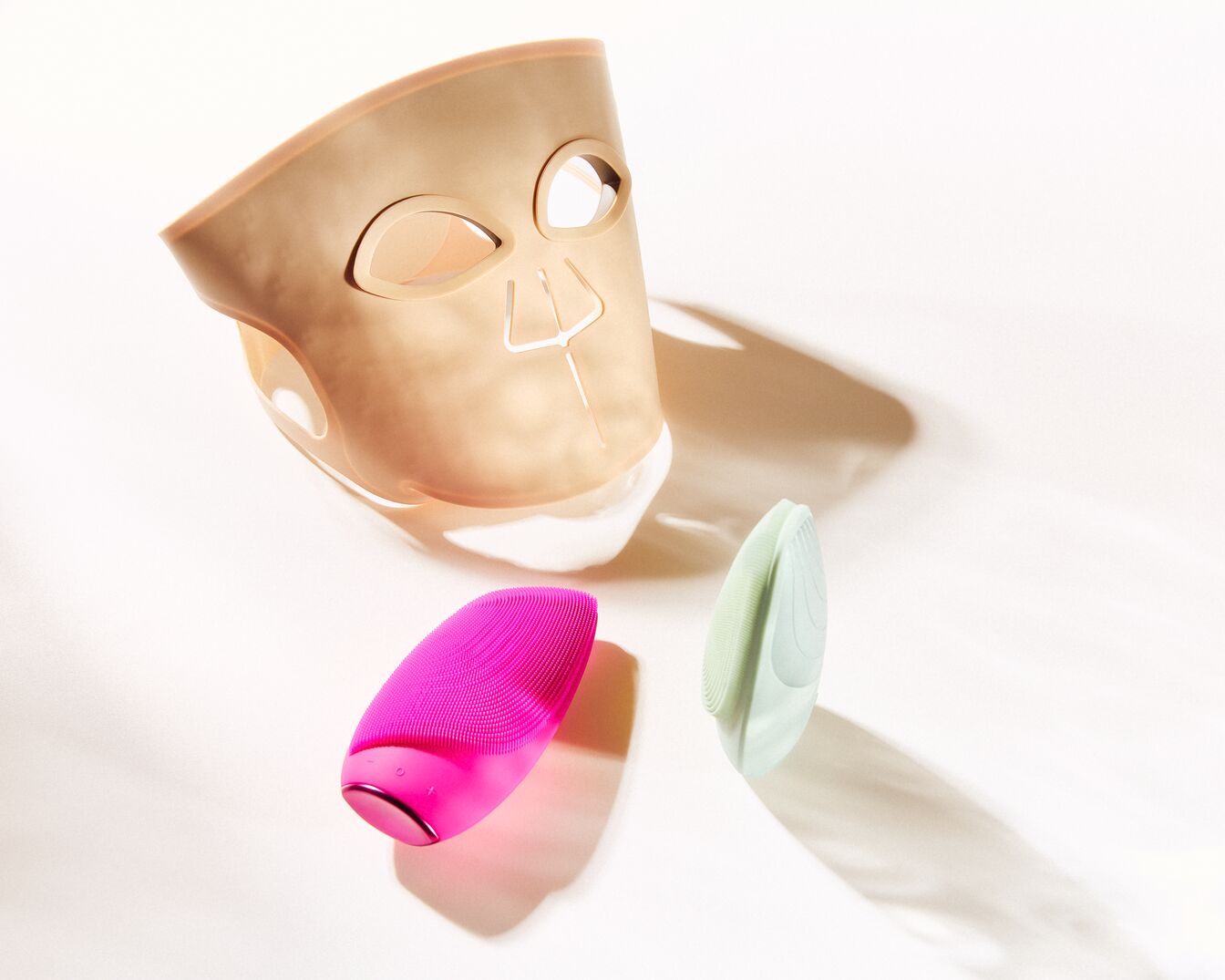 Découvrez le masque facial beige futuriste avec des ouvertures pour les yeux et le nez, accompagné de brosses nettoyantes roses et vertes pour une peau éclatante.