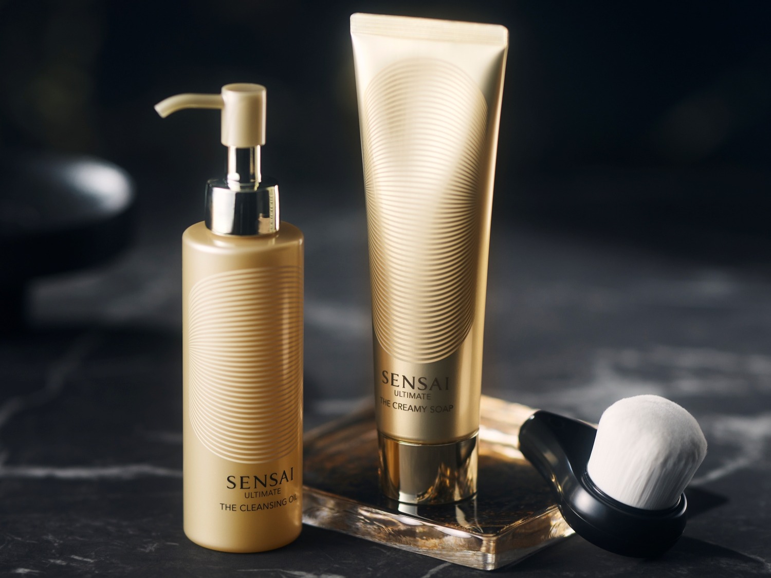 Découvrez le luxe ultime avec l'huile nettoyante Sensai Ultimate, le savon crémeux et la brosse douce pour une peau éclatante.