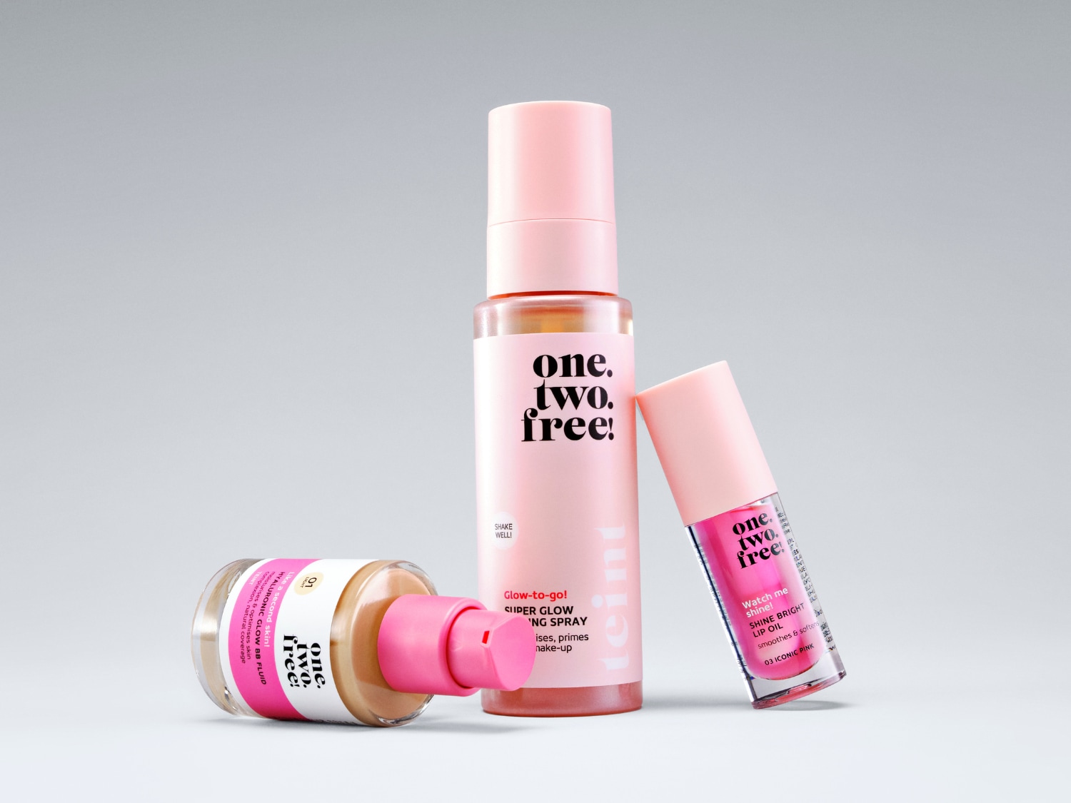 Drei One.Two.Free!-Produkte in rosa Verpackung: Hyaluronic Glow BB Fluid, Super Glow Setting Spray und Shine Bright Lip Oil.
