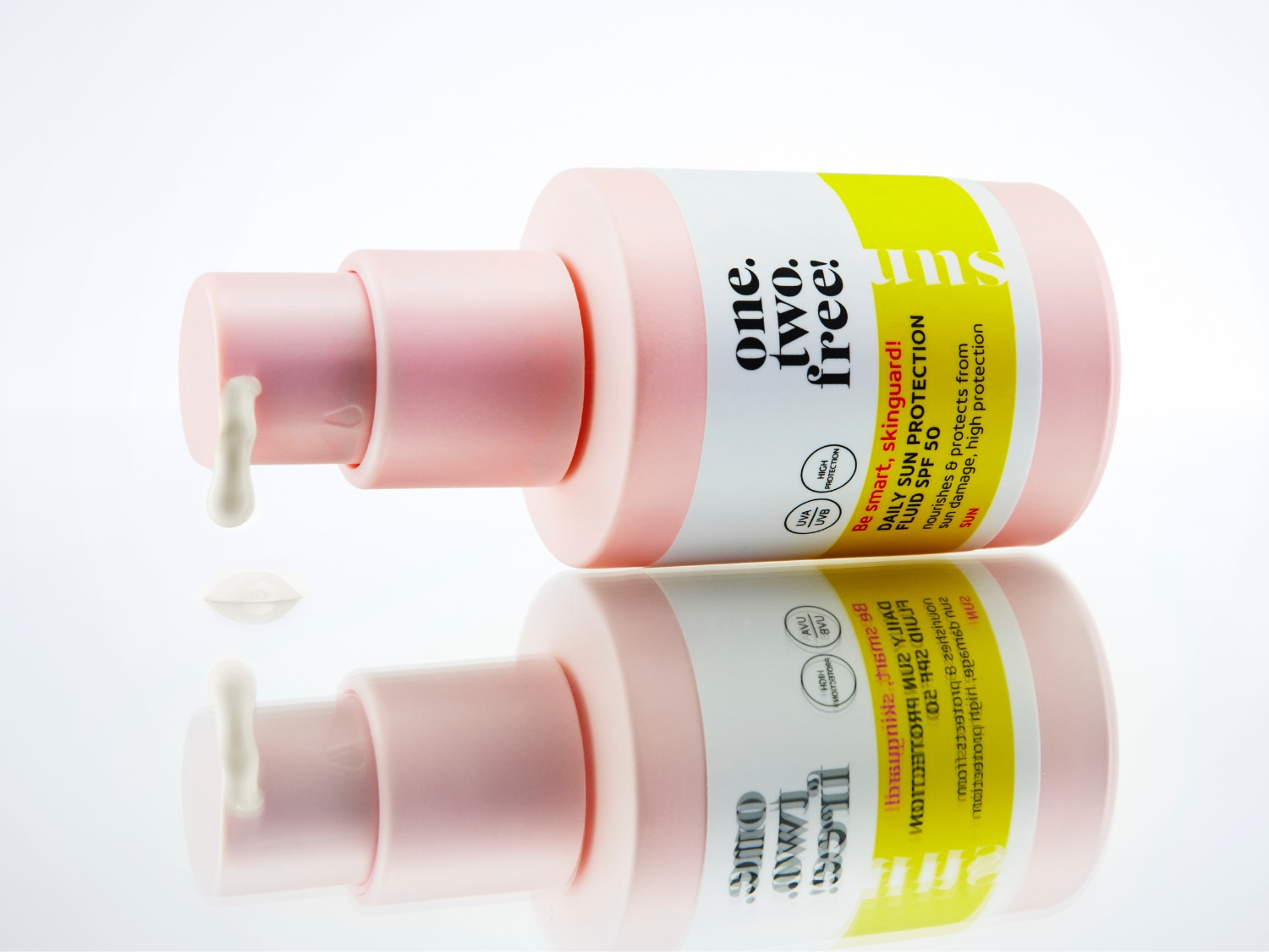 Die rosa Flasche "one.two.free!" Daily Sun Protection Fluid SPF 50 mit gelbem Etikett liegt auf einer reflektierenden Oberfläche, ein Tropfen der weißen Flüssigkeit hängt an der Pumpe.