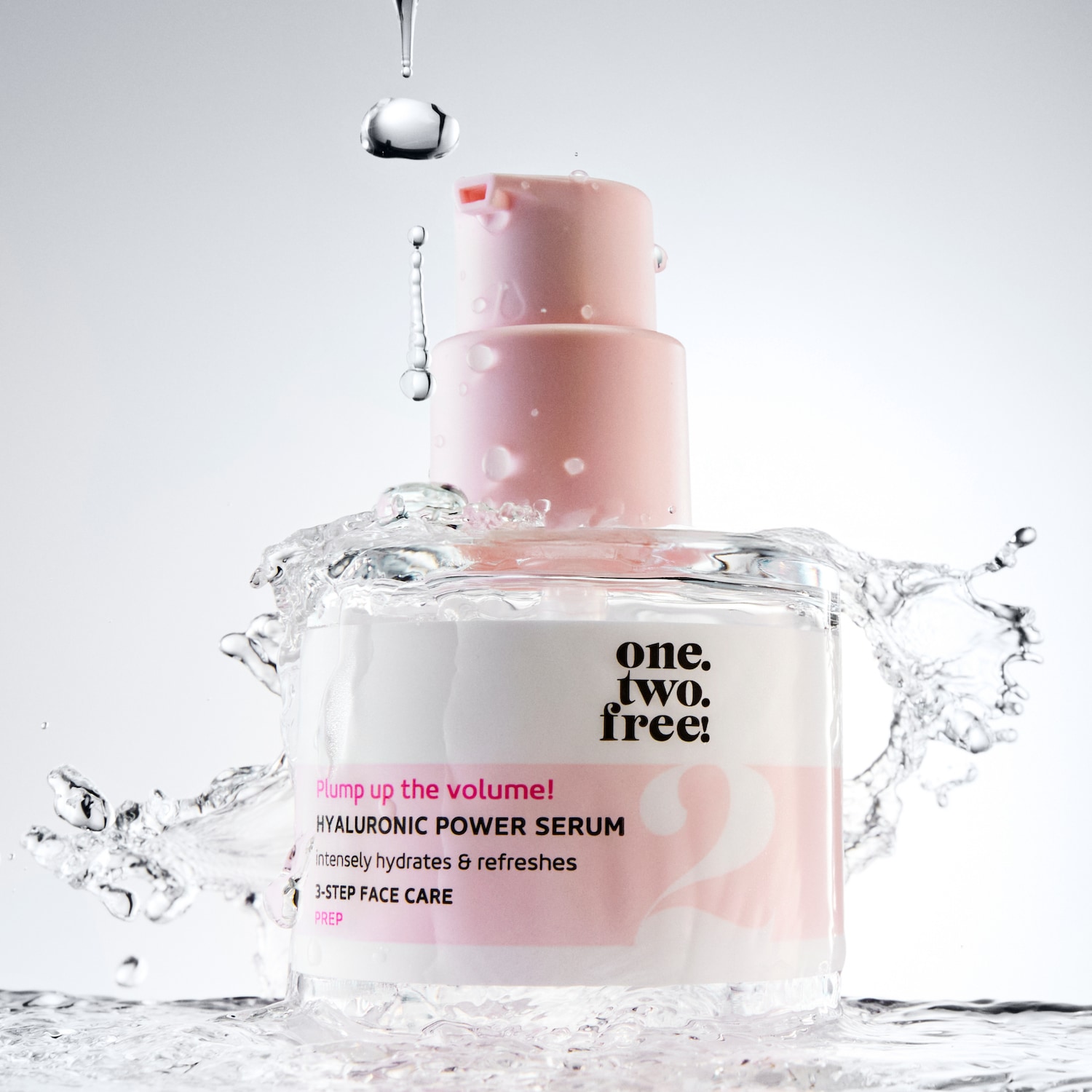 Serum do twarzy One Two Free! Hyaluronic Power Serum w przezroczystej butelce z różowymi akcentami, otoczony rozpryskującą się wodą, obiecuje intensywne nawilżenie i odświeżenie.