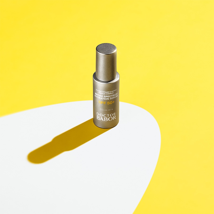 Nahaufnahme einer Doctor Babor Broad Spectrum Hydration Serum SPF 50+ Flasche in einer goldenen Verpackung vor einem gelben Hintergrund.