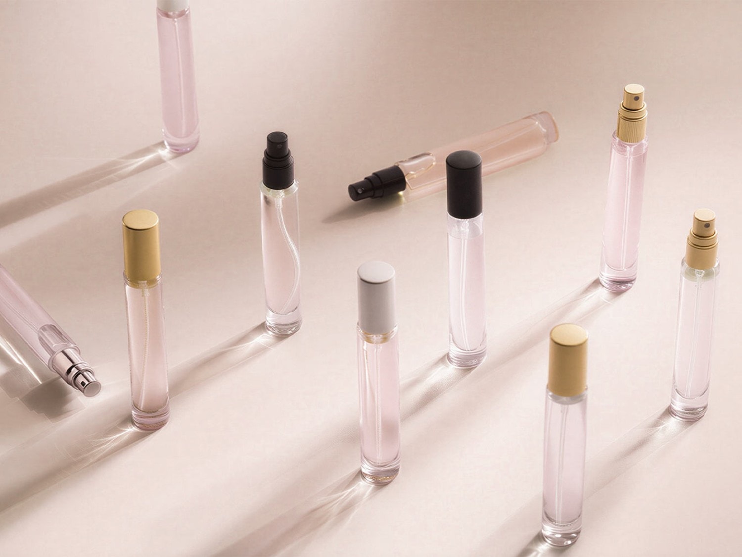Verschiedene Parfümflakons mit silbernen, goldenen und schwarzen Kappen sind auf einem hellen Hintergrund angeordnet.