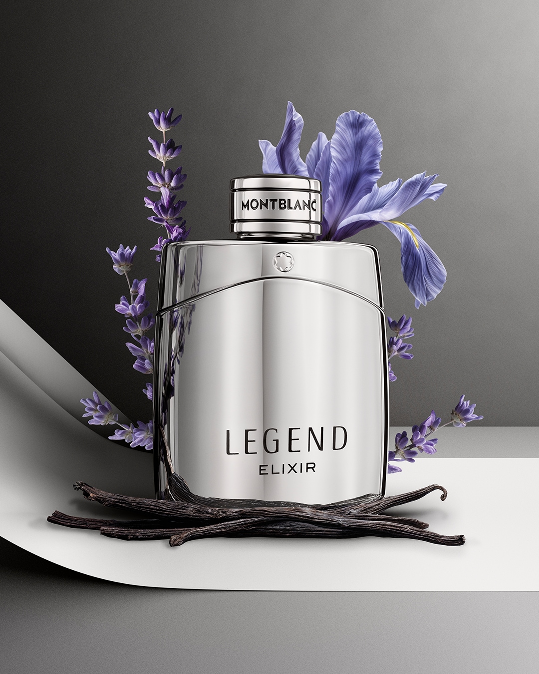 Błyszczący srebrny flakon perfum Montblanc Legend Elixir otoczony jest fioletowymi kwiatami i laskami wanilii, co dodaje mu elegancji i głębi.