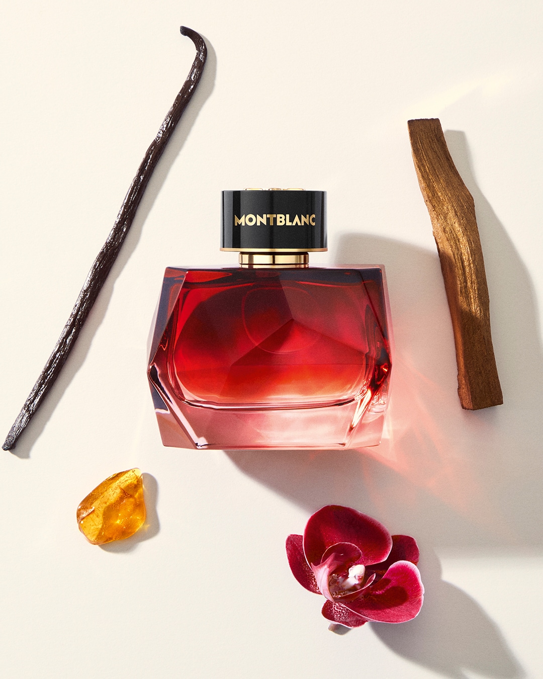 Butelka Montblanc o pojemności 100 ml ma gradientowy czerwony odcień, który przechodzi od jasnego do ciemnego, z czarną zakrętką ozdobioną złotym napisem Montblanc, obok niej leży laska wanilii, kawałek bursztynu, orchidea i kawałek drewna.