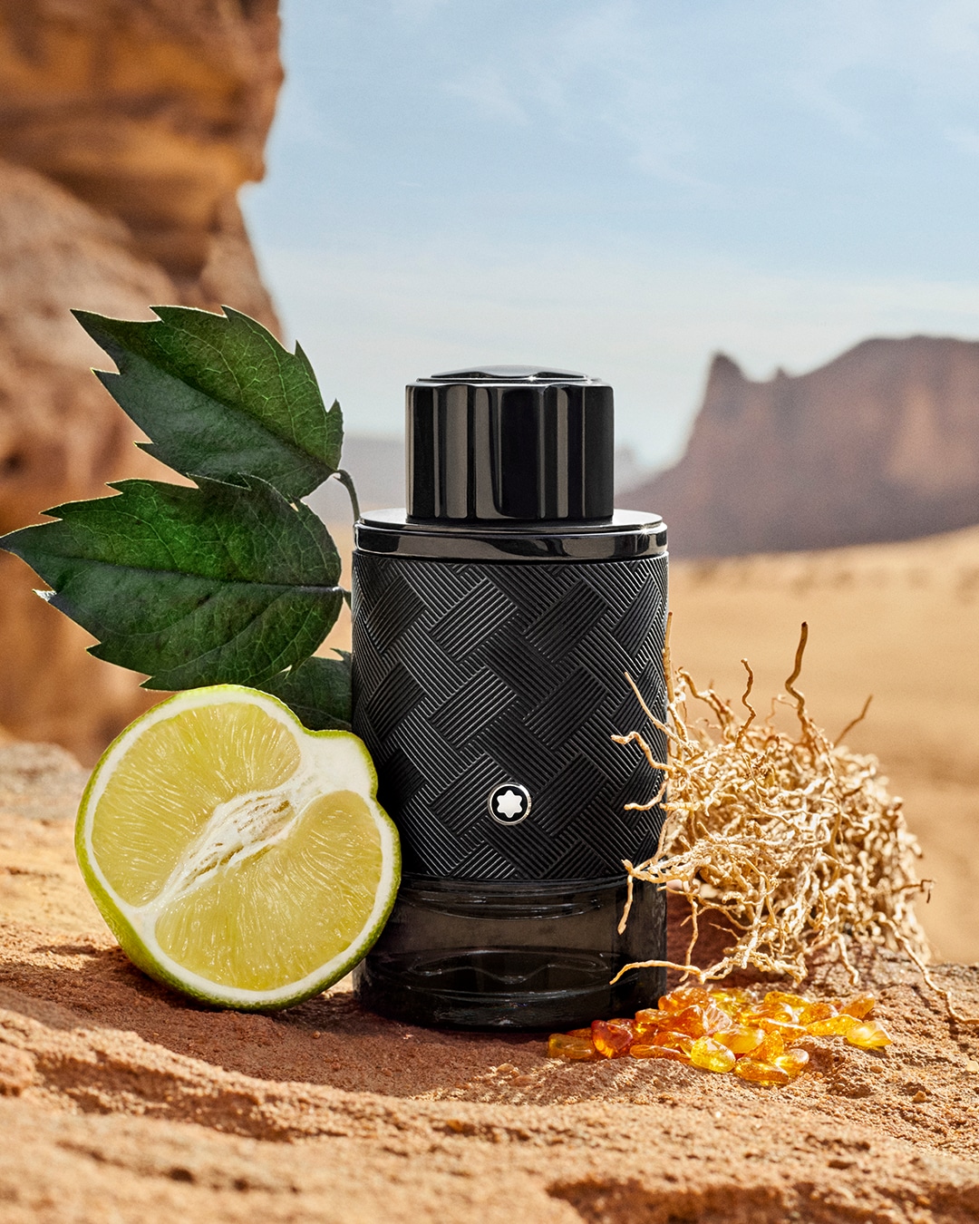 Czarny flakon Montblanc z teksturą, limonka i bursztyn na tle pustynnego krajobrazu tworzą bogatą kompozycję.