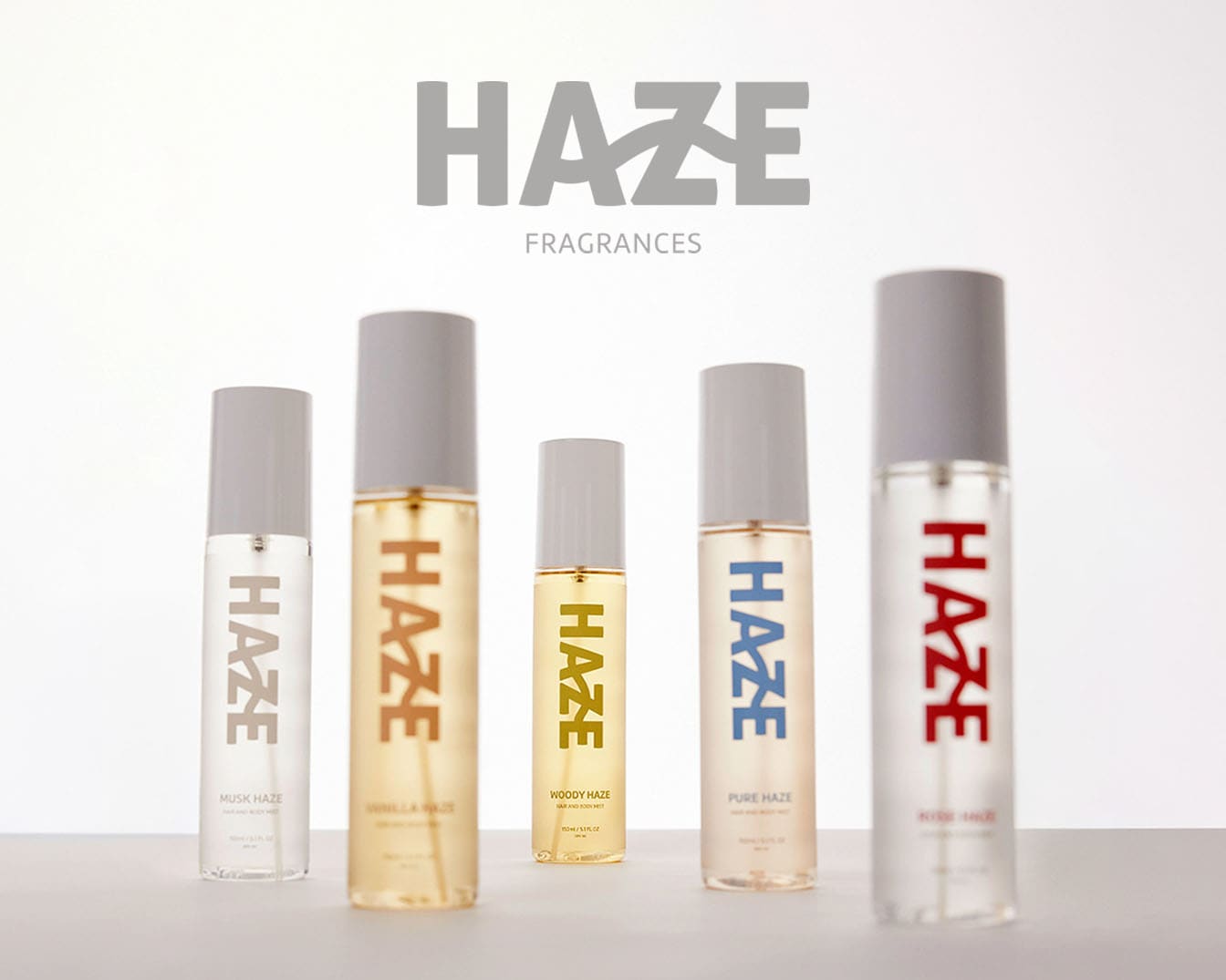 Scopri la collezione di fragranze Haze, che include Musk Haze, Vanilla Haze, Woody Haze, Pure Haze e Kiss Haze, ognuna in flaconi spray trasparenti con tappi grigi.