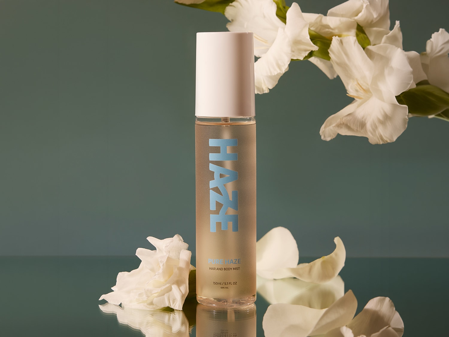 Ecco una bottiglia di spray per capelli e corpo Pure Haze, con scritte blu su sfondo trasparente, tappo bianco e decorata con fiori bianchi.