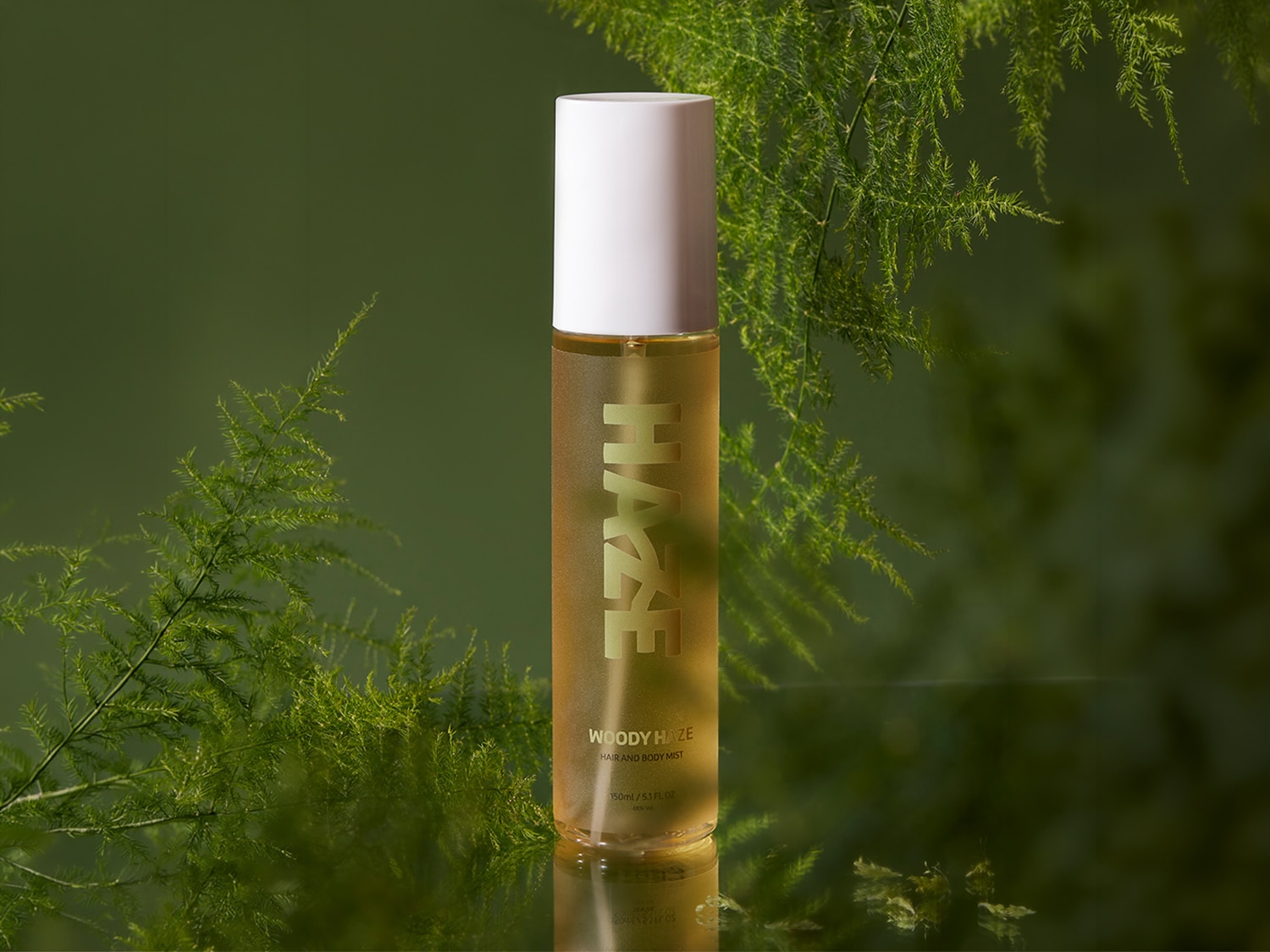 Ecco la bruma per capelli e corpo Woody Haze in un flacone trasparente con tappo bianco, che rivela una tonalità dorata, ideale per rinfrescarti con un profumo delicato.