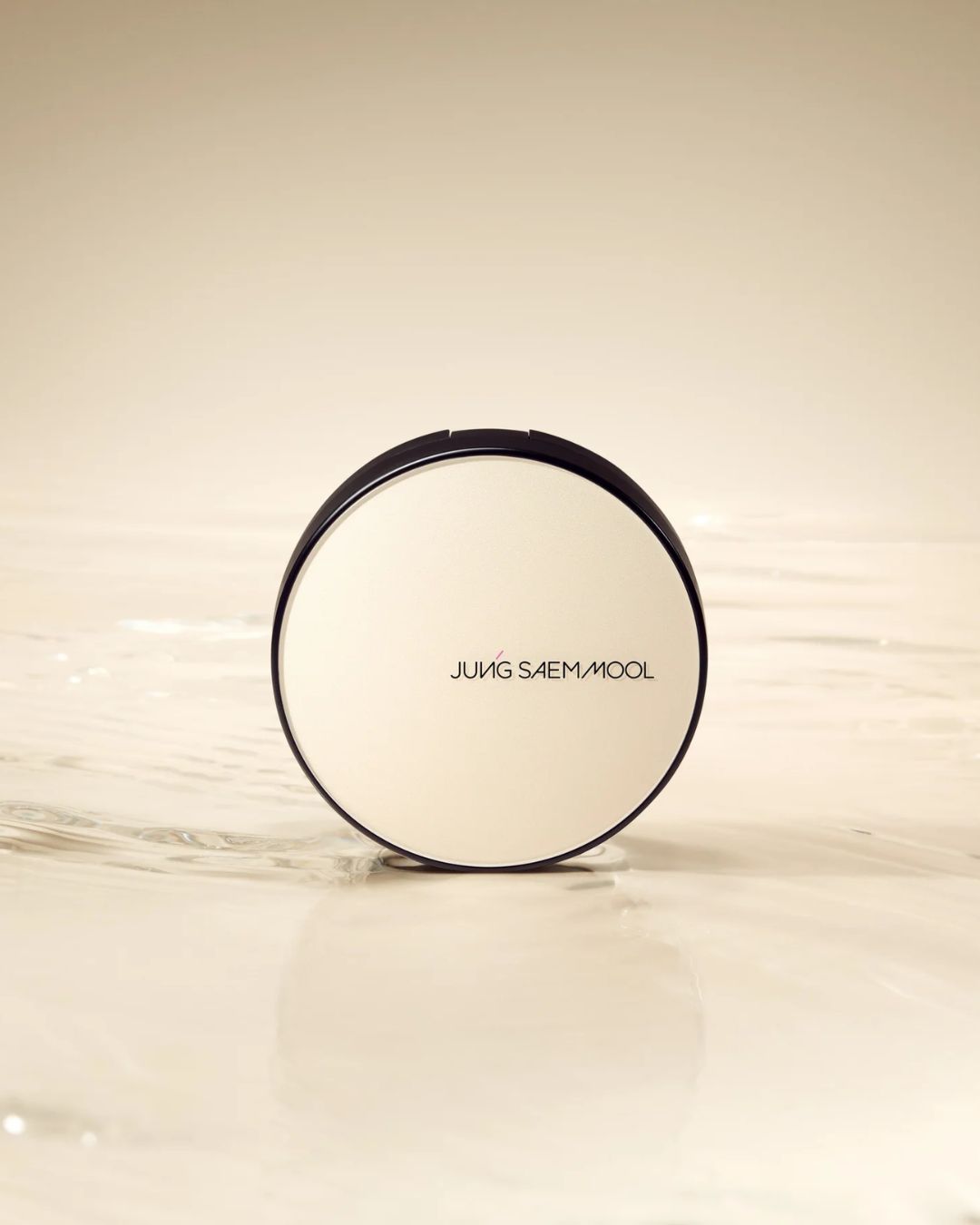 Puder do twarzy Jung Saem Mool w okrągłym, kremowym opakowaniu z czarnymi brzegami, stojący na błyszczącej powierzchni.