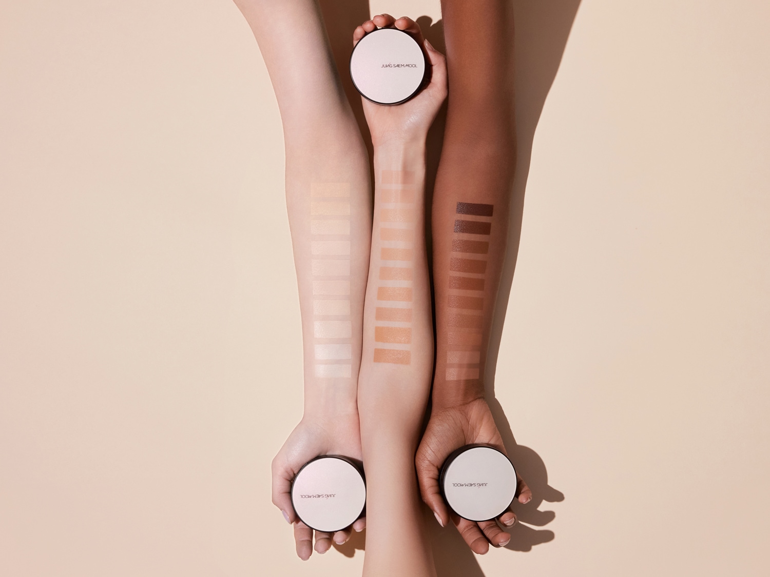 Trzy odcienie skóry prezentują różne próbki podkładu Jung Saem Mool, od jasnych po ciemne, z okrągłymi opakowaniami produktu w dłoniach.