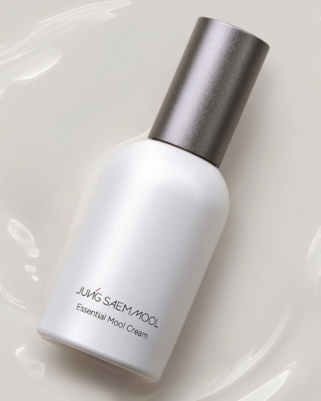 Biała butelka kremu Jung Saem Mool Essential Mool z szarym aplikatorem na tle białej, kremowej substancji.