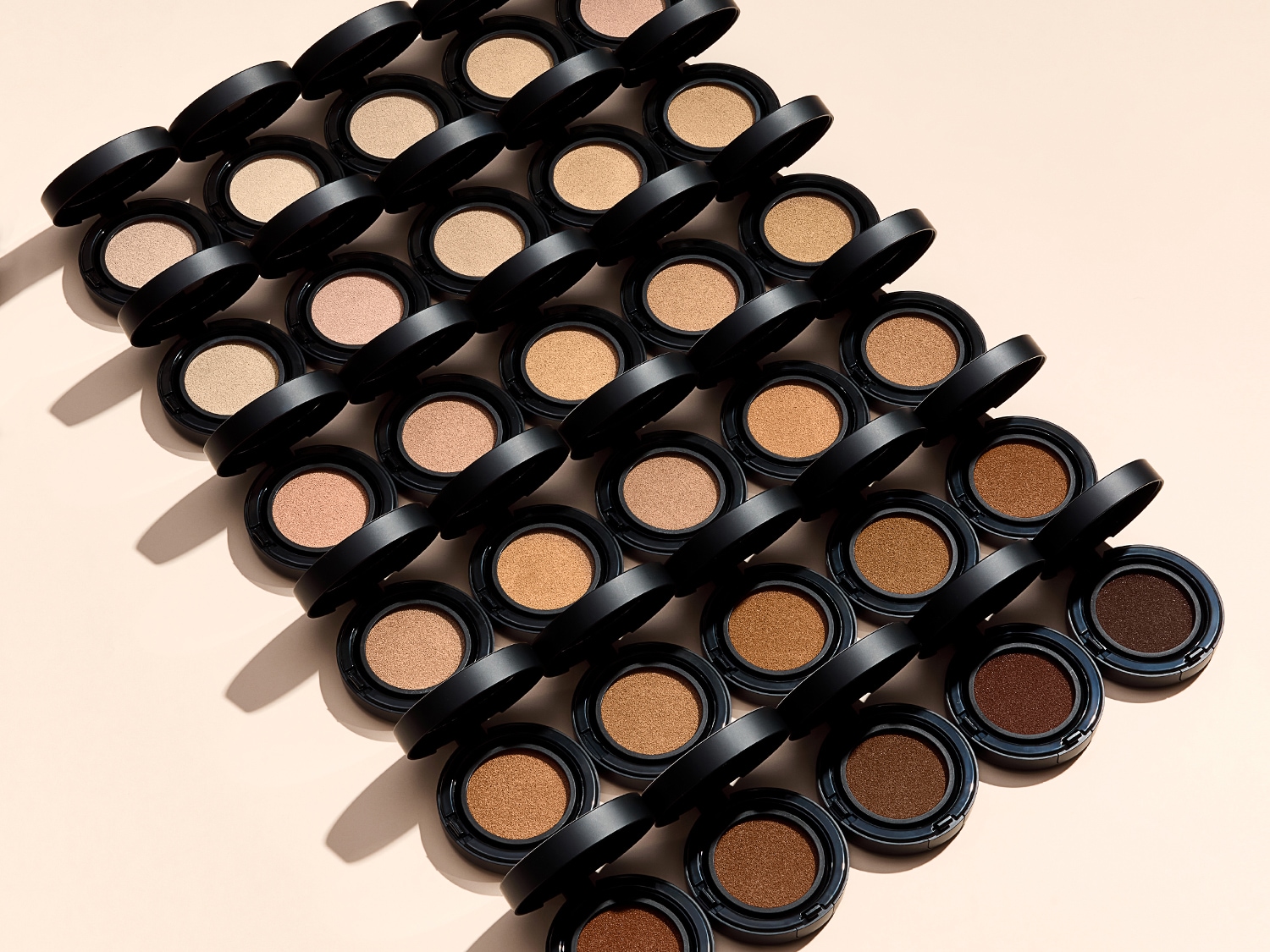 Różne odcienie podkładu w kompaktach z czarnym wieczkiem, ułożone w rzędach od najjaśniejszego do najciemniejszego, tworzą efekt ombre.