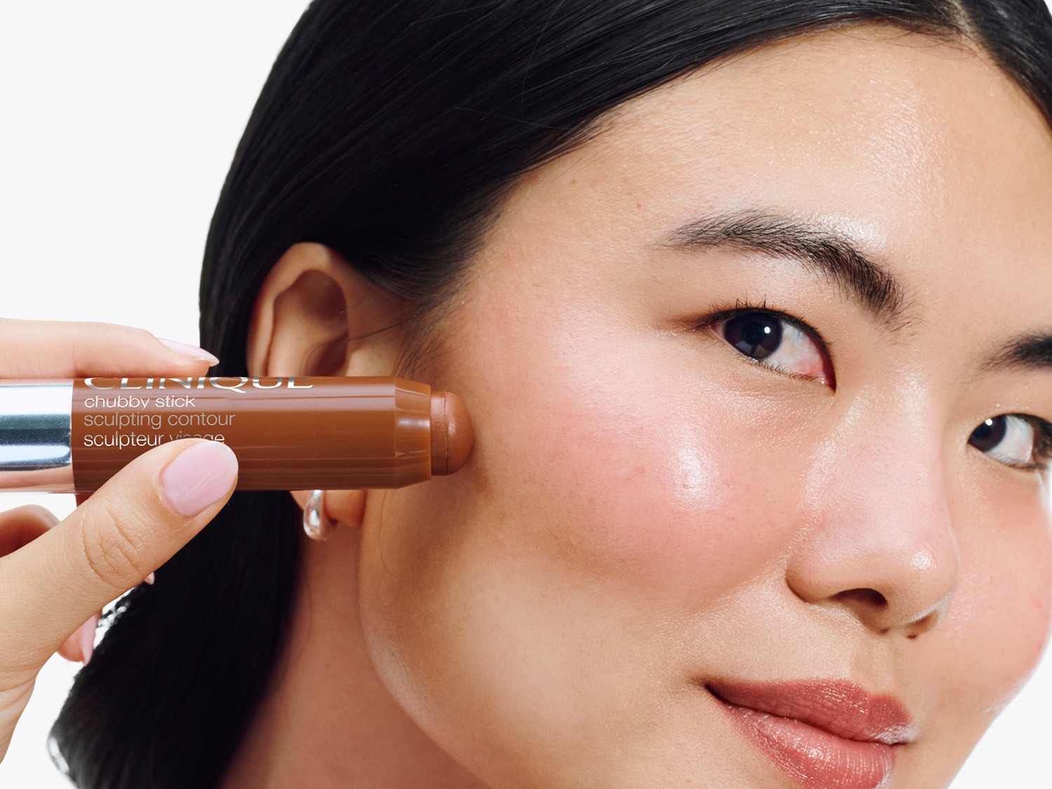 Une femme utilise un bâton de contouring Clinique Chubby Stick brun pour sculpter ses pommettes, créant un look défini et éclatant.