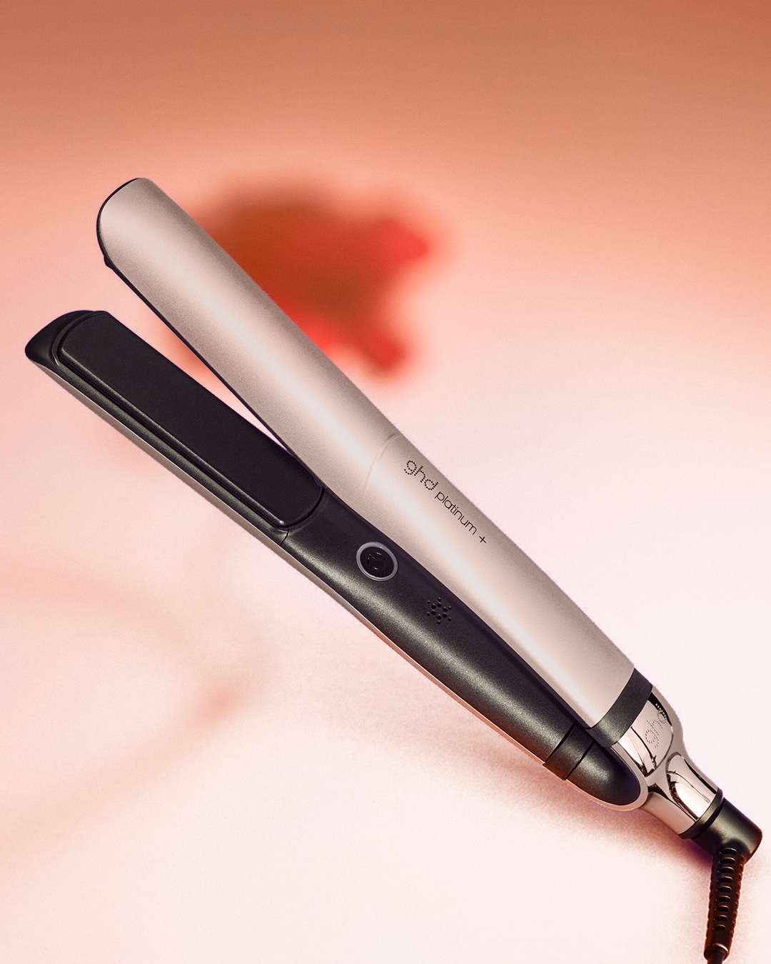 Voici un fer à lisser ghd platinum+ avec un corps rose clair et des plaques noires, conçu pour coiffer les cheveux en douceur.