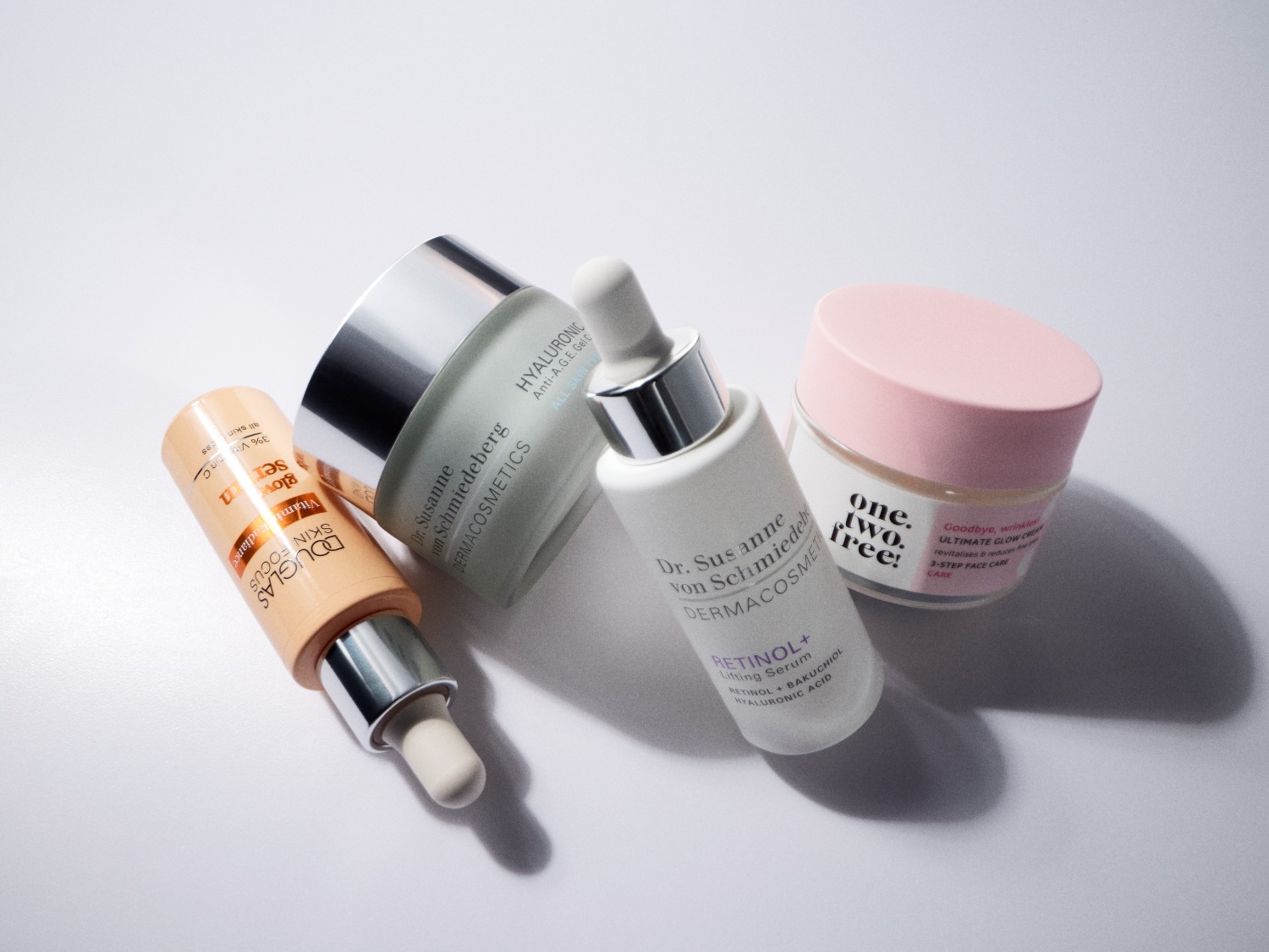 Cztery produkty do pielęgnacji skóry, w tym serum Douglas Skin Focus z 3% witaminą C, żel Dr. Susanne von Schmiedeberg z kwasem hialuronowym, serum liftingujące Retinol+ oraz krem One.Two.Free! Ultimate Glow.