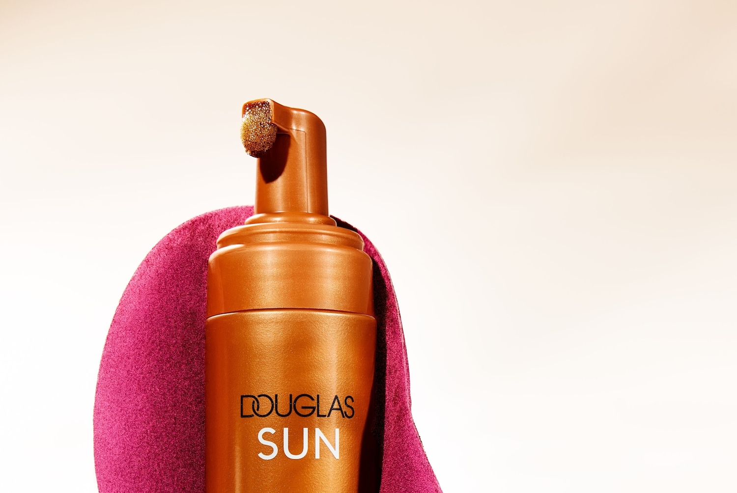 Le flacon bronze de Douglas Sun, coiffé d'un embout mousse doré, promet un hâle ensoleillé, le tout enveloppé dans un tissu fuchsia doux.
