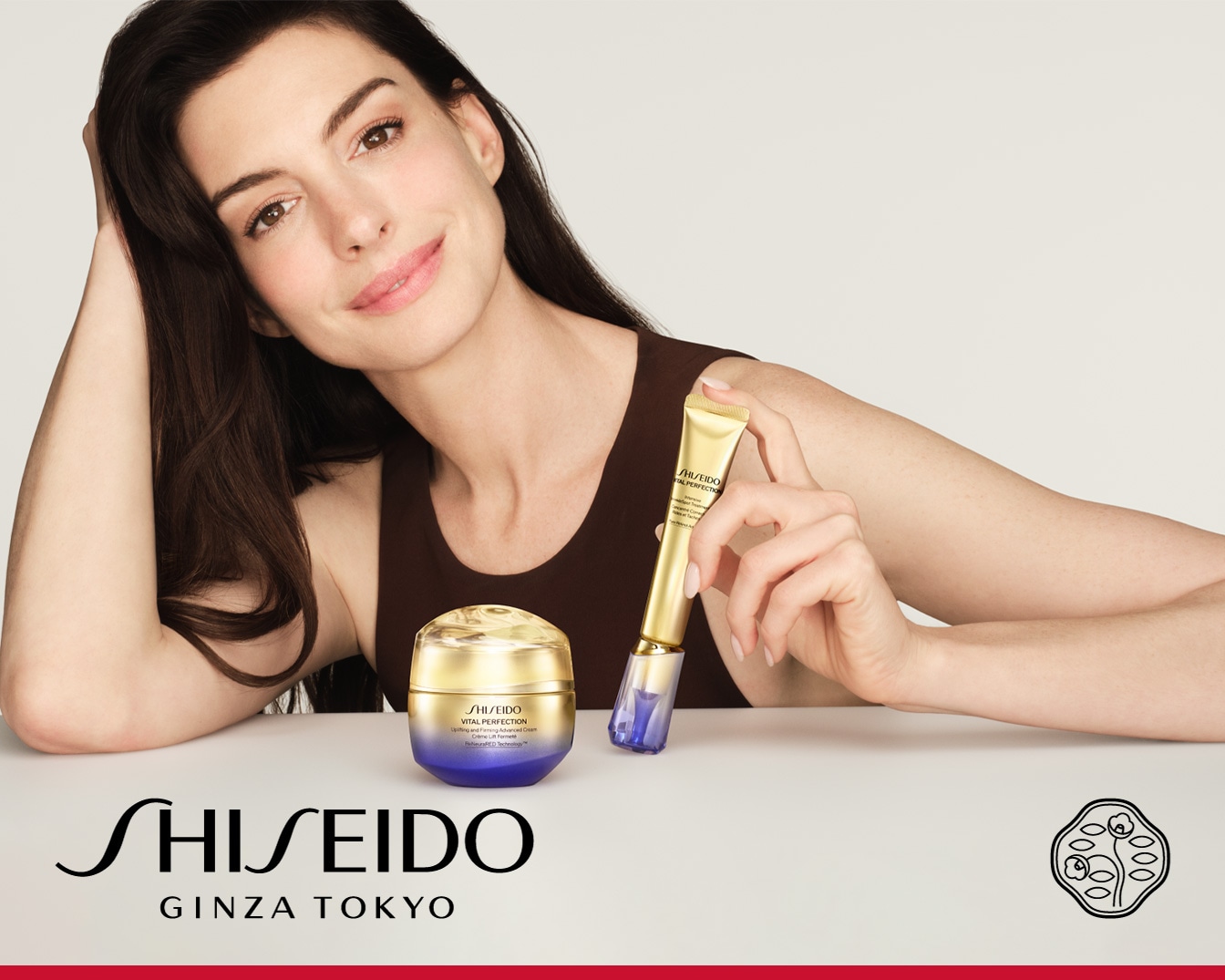 Anne Hathaway präsentiert Shiseido Vital Perfection: eine goldene Creme in einem violetten Tiegel und eine goldene Tube mit blauem Applikator für eine strahlende, perfektionierte Haut.