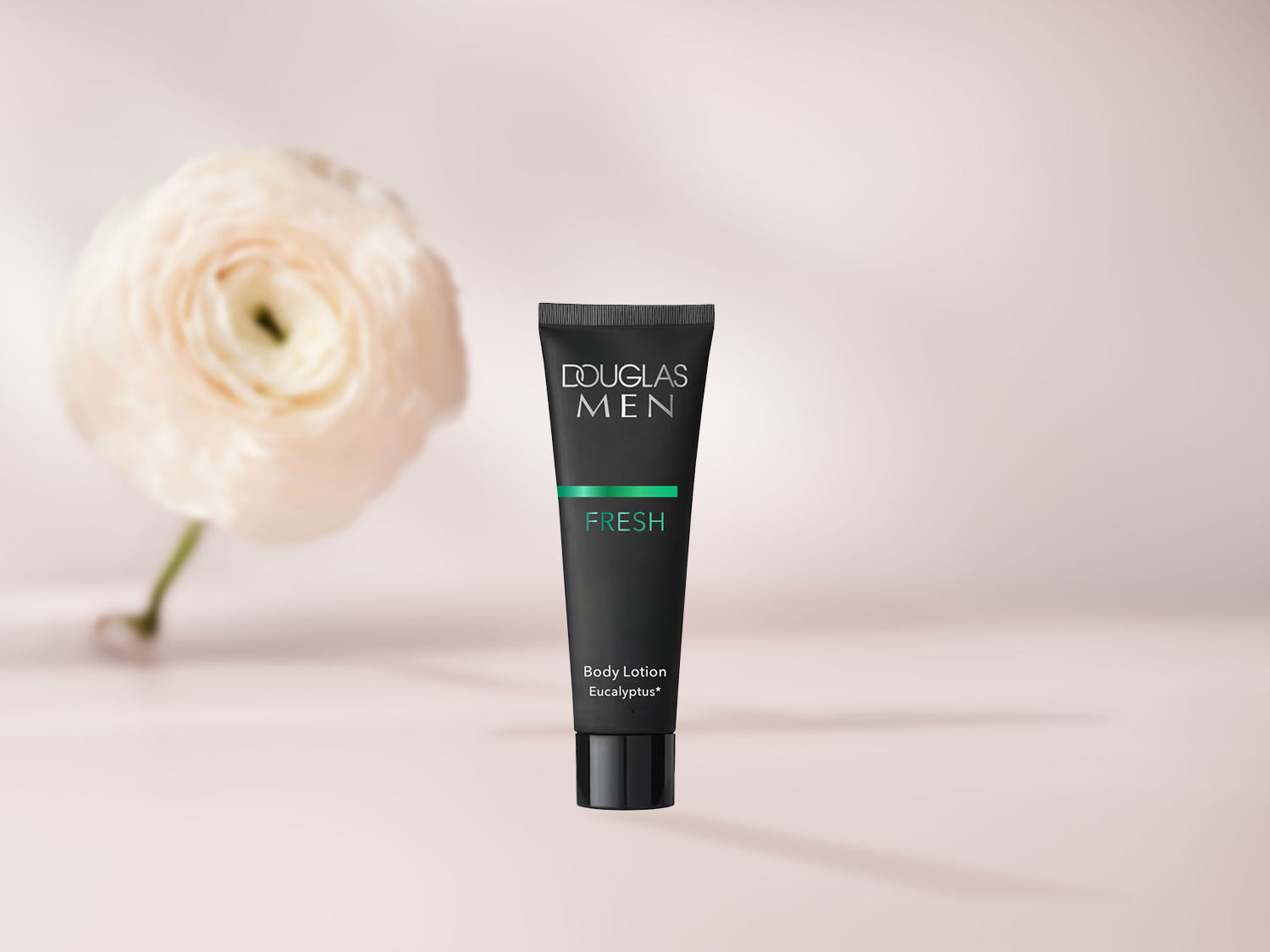 Douglas Men Fresh Bodylotion Eukalyptus in einer schwarzen Tube mit grünem Akzent, daneben eine zarte, helle Blume.