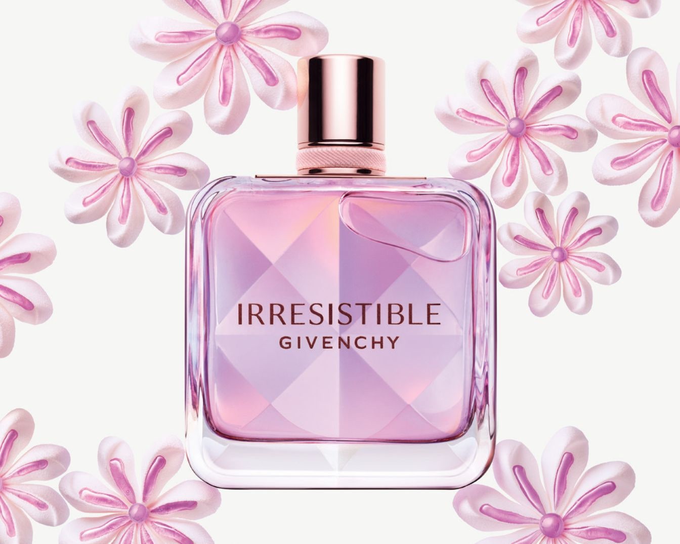 Quadratischer Glasflakon von Givenchy Irresistible, gefüllt mit rosa Flüssigkeit, umgeben von weißen Blumen mit rosa Akzenten.
