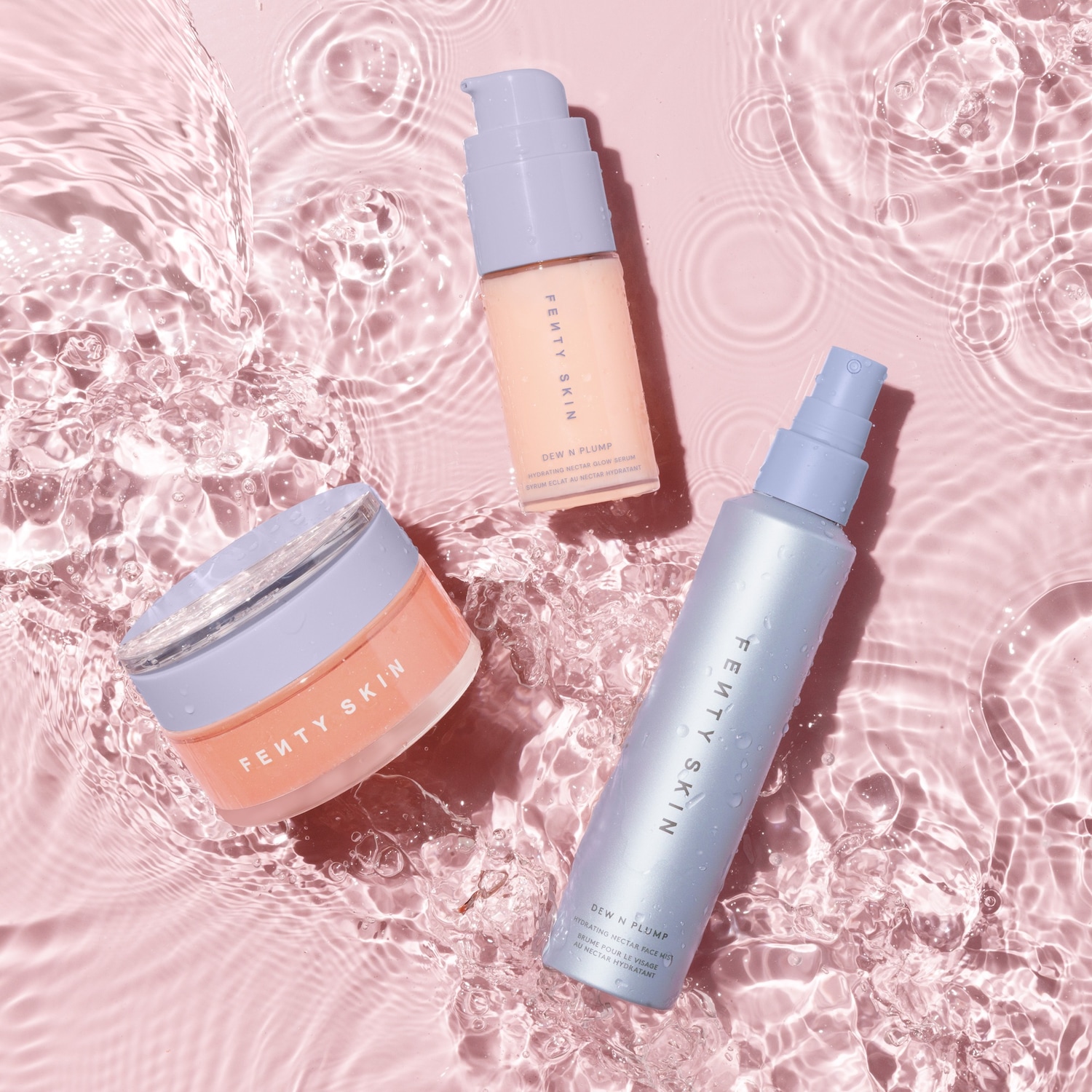 Drie Fenty Skin Dew N Plump producten liggen in helder water: een serum in een perzikkleurige flacon, een gezichtsspray in een blauwe flacon en een crème in een perzikkleurige pot.