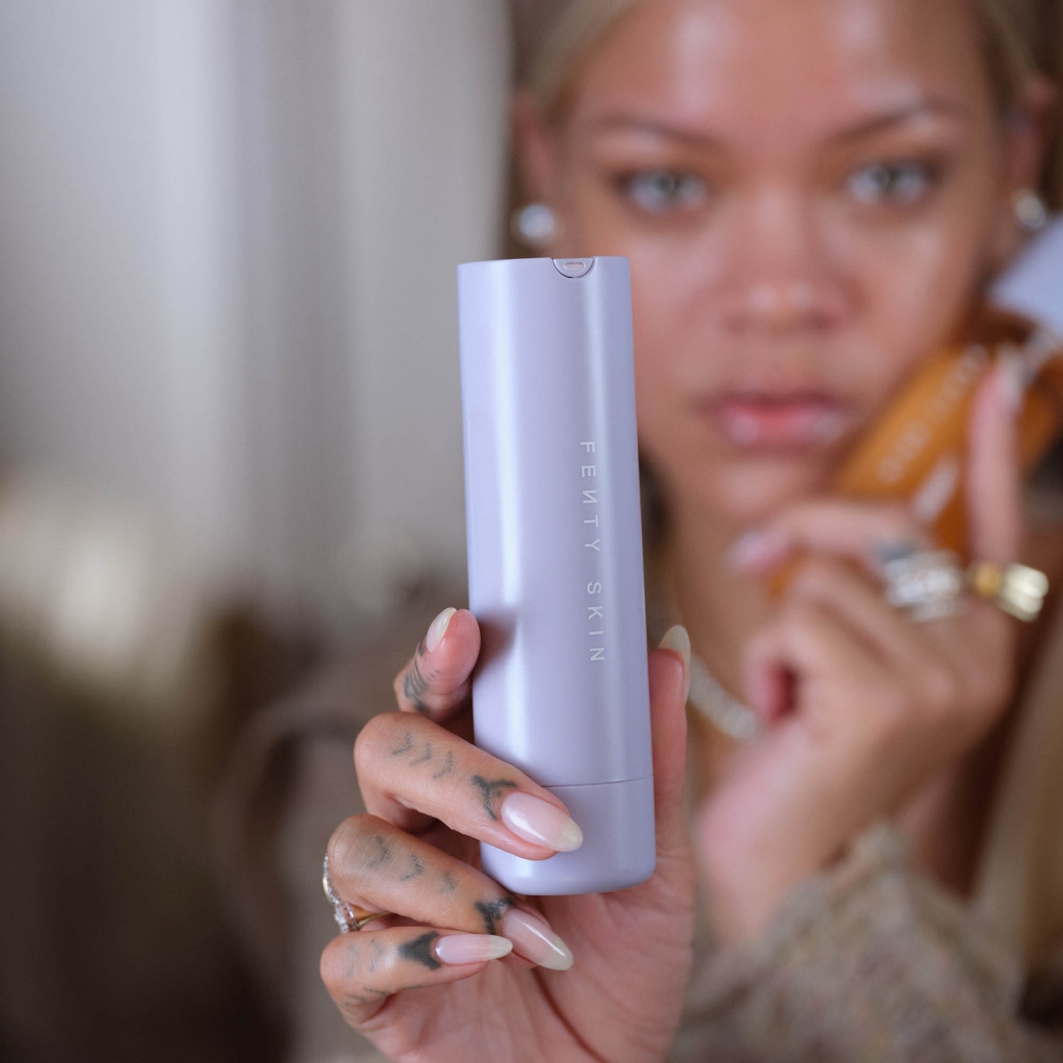 Een vrouw houdt een lichtpaarse Fenty Skin-tube vast, de verpakking is minimalistisch en strak.