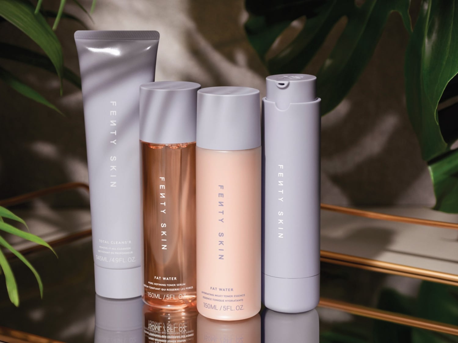 Vier Fenty Skin producten staan op een spiegelende ondergrond, waaronder een Total Cleans'r, twee Fat Water toners en een hydraterende milky toner essence, allemaal in zachte, pastelkleurige verpakkingen.