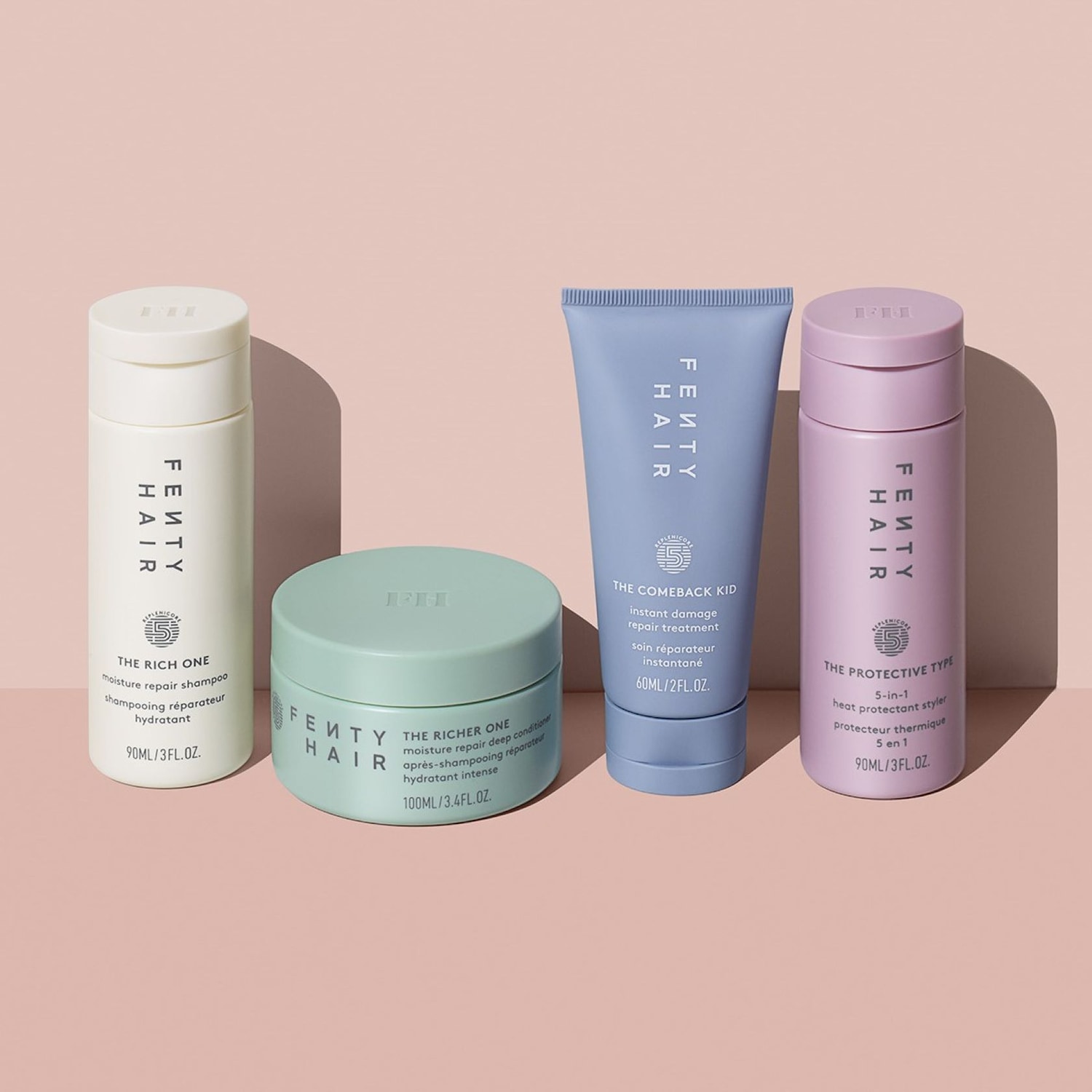 Vier Fenty Hair-producten staan op een rij: een witte shampoo, een groene conditioner, een blauwe haarbehandeling en een paarse heat protectant styler.
