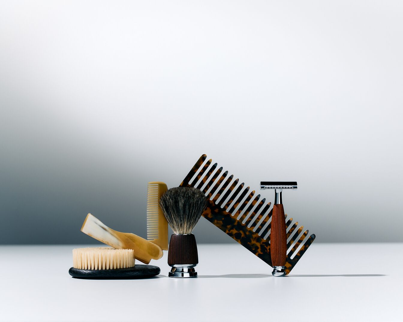 Verschiedene Herrenpflegeprodukte, darunter Bürsten, Kämme und ein Rasierer, sind auf einem hellen Untergrund angeordnet.