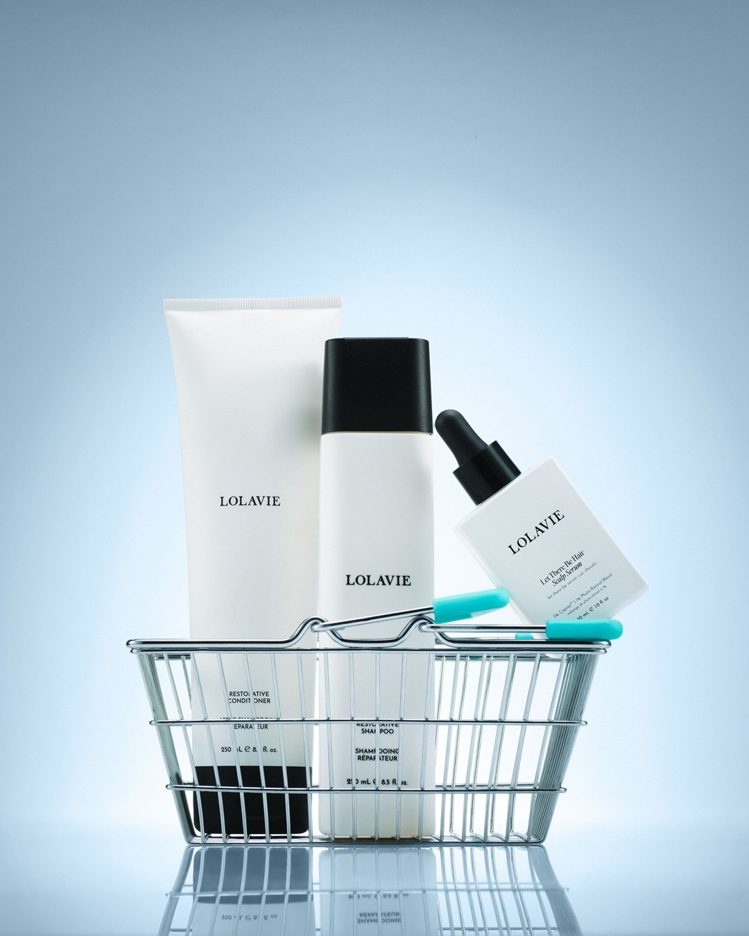 In einem silbernen Einkaufskorb befinden sich Lolavie-Haarpflegeprodukte, darunter eine Spülung, ein Shampoo und ein Kopfhautserum in weißen Flaschen.